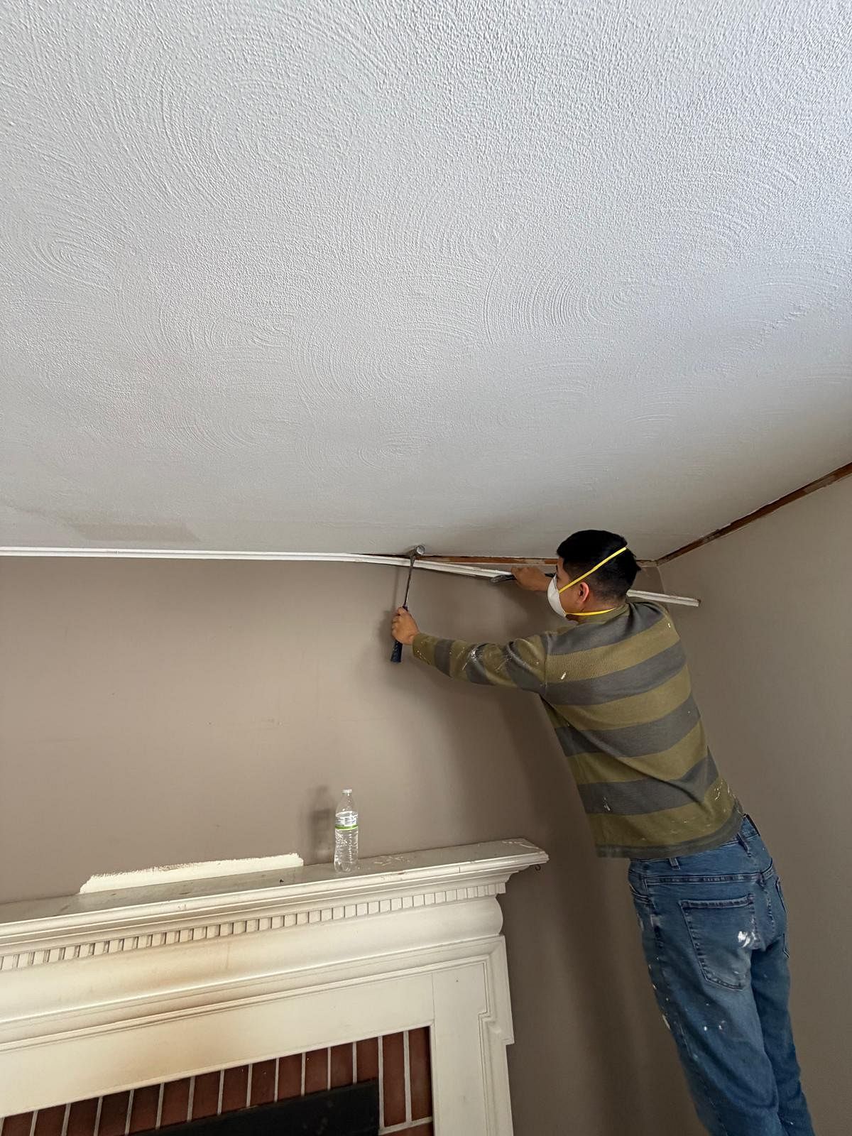 Person installing trim along a ceiling corner above a fireplace in a room.