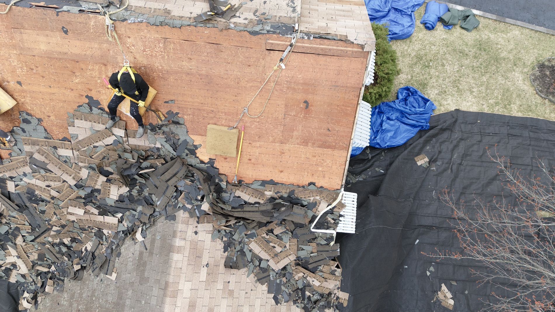 Roofing work on a damaged roof beside a brick wall, with black tar paper and blue gloves nearby