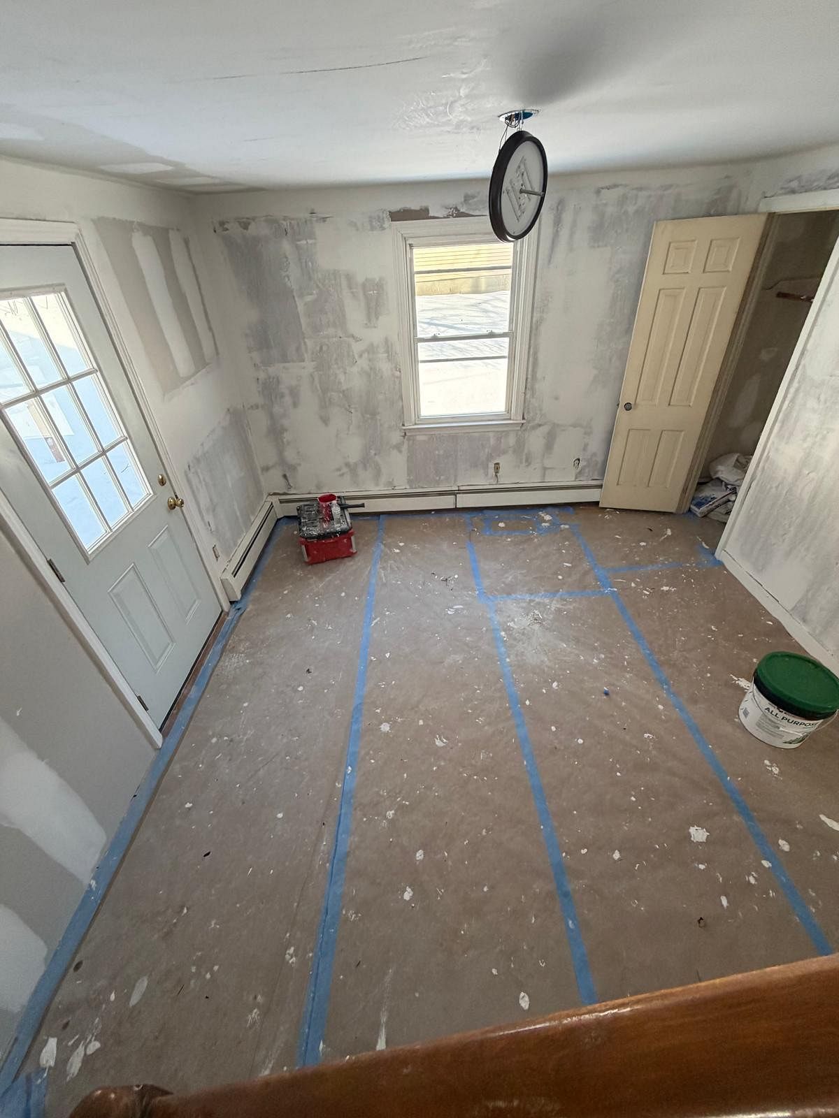Empty room under renovation with taped floor, bare walls, a window, and paint buckets.