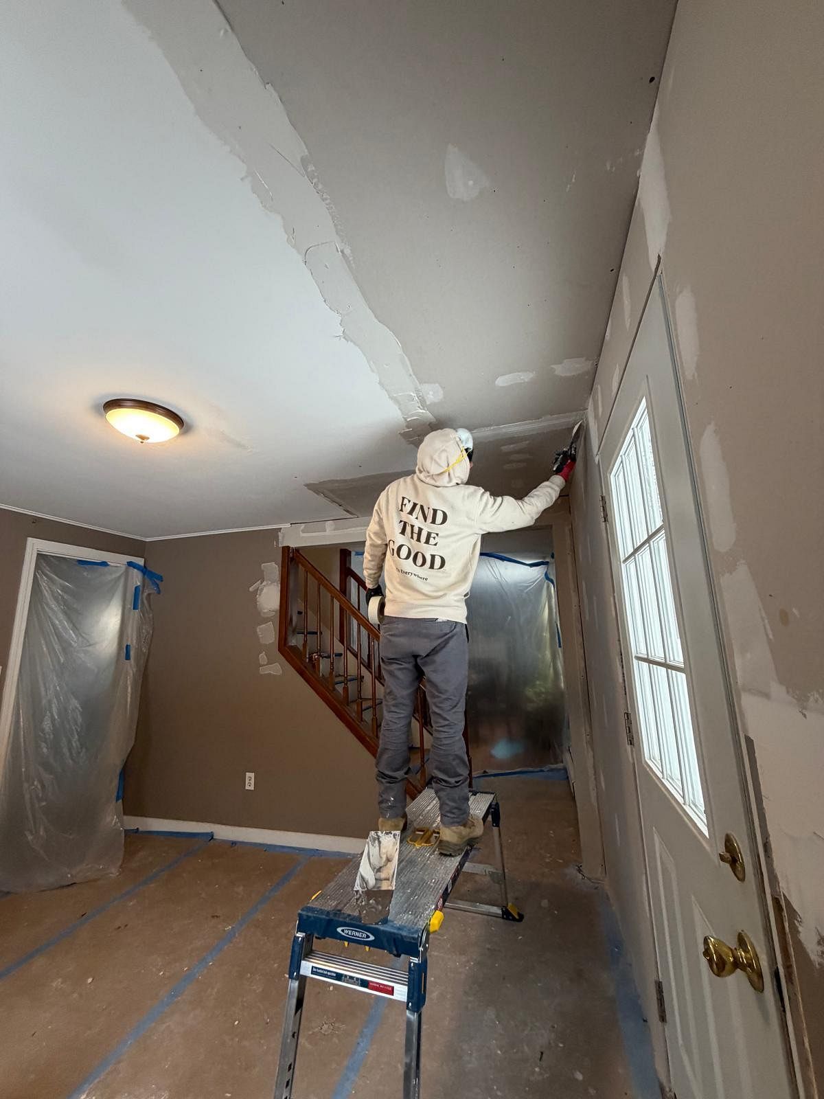 Person standing on a ladder painting a hallway ceiling during home renovation.