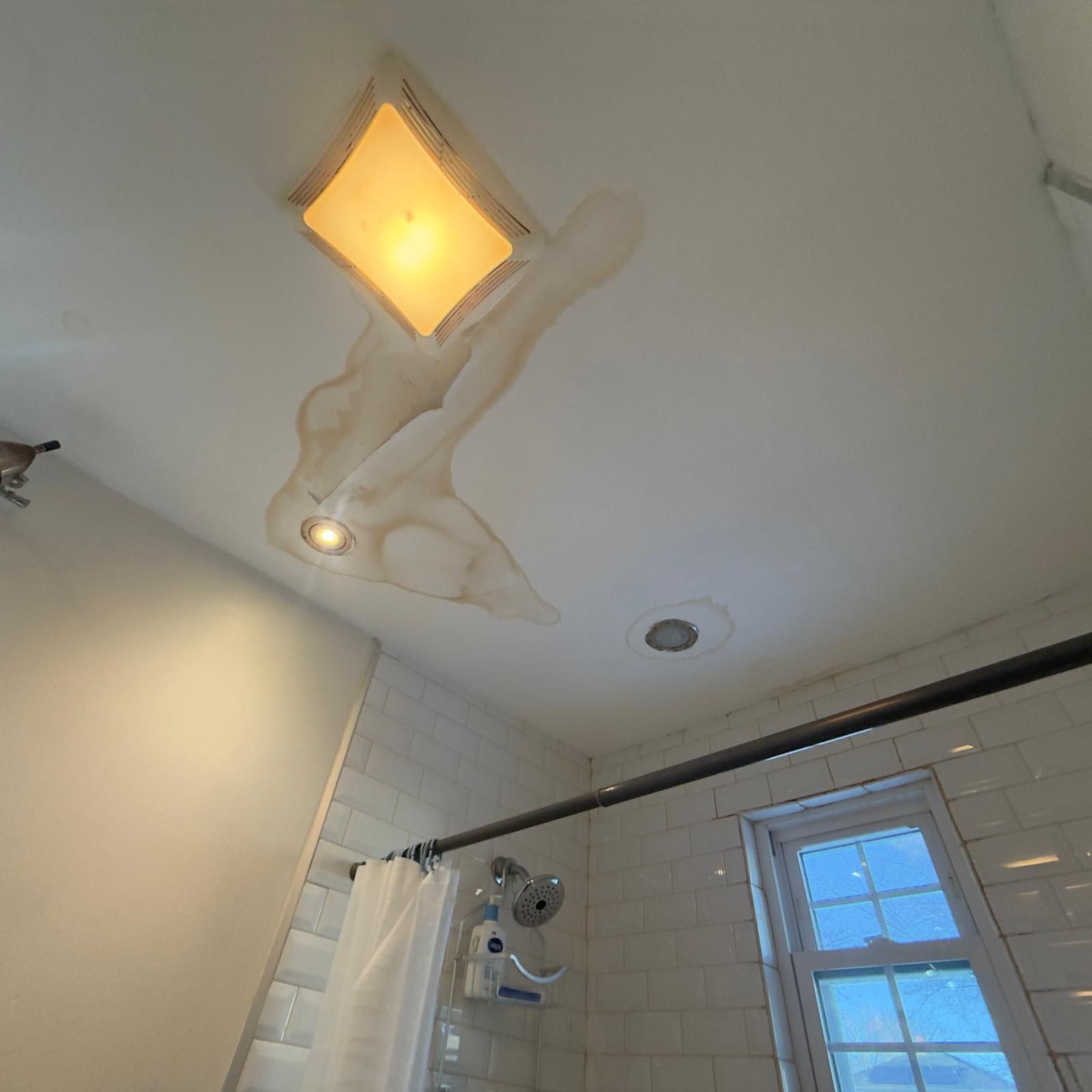 Bathroom ceiling with a glowing light fixture, water stains, and a shower curtain below