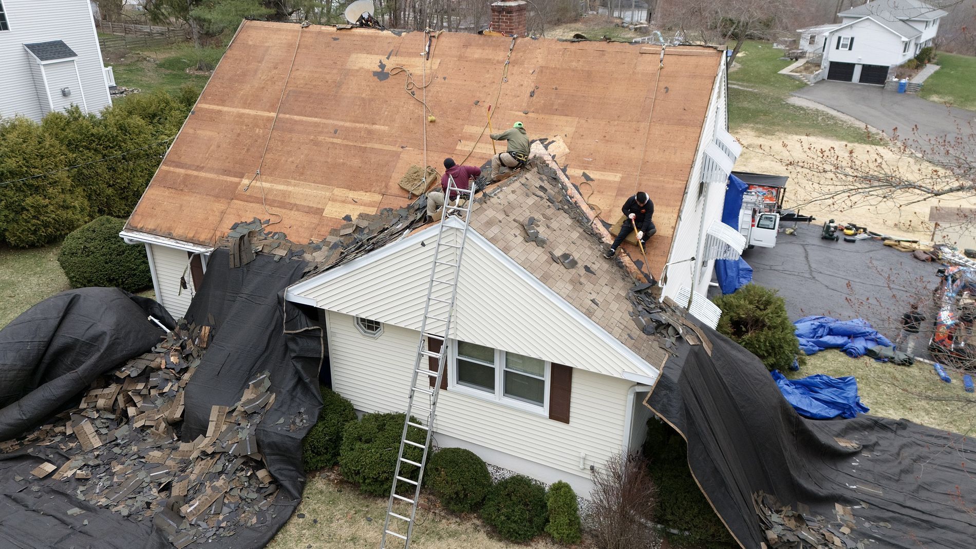 House with roof and front wall collapsed by severe storm damage, debris and tarp covering the sides