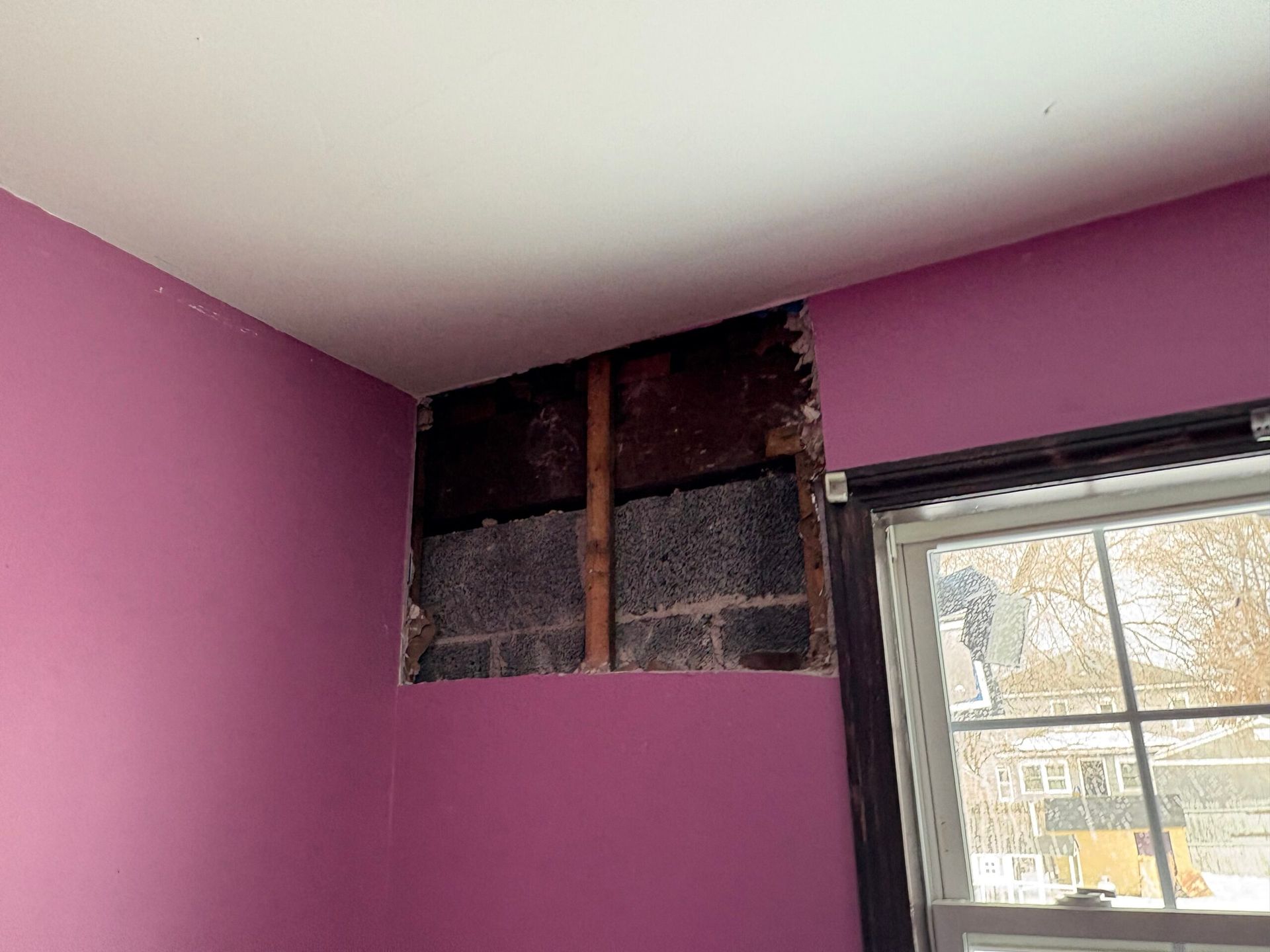 Partially stripped purple wall corner with exposed dark insulation near a window