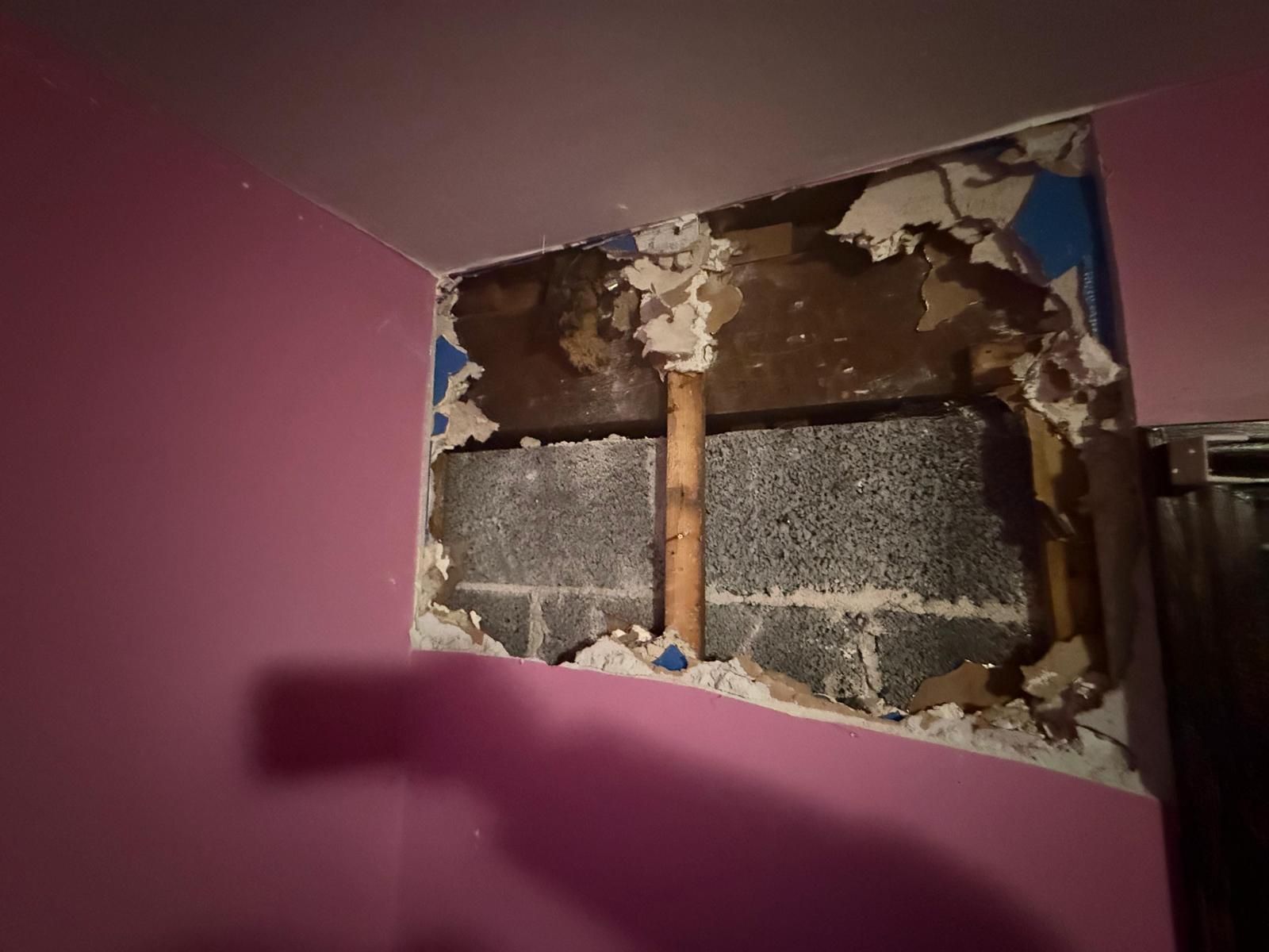 Damaged wall with exposed pipe, cracked plaster, and peeling paint in a purple room