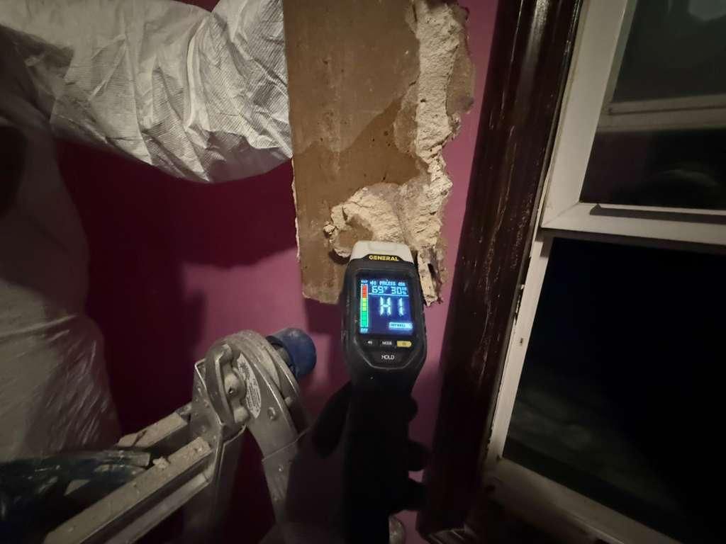 Broken wall with peeling plaster beside a lit handheld device in a dim bedroom