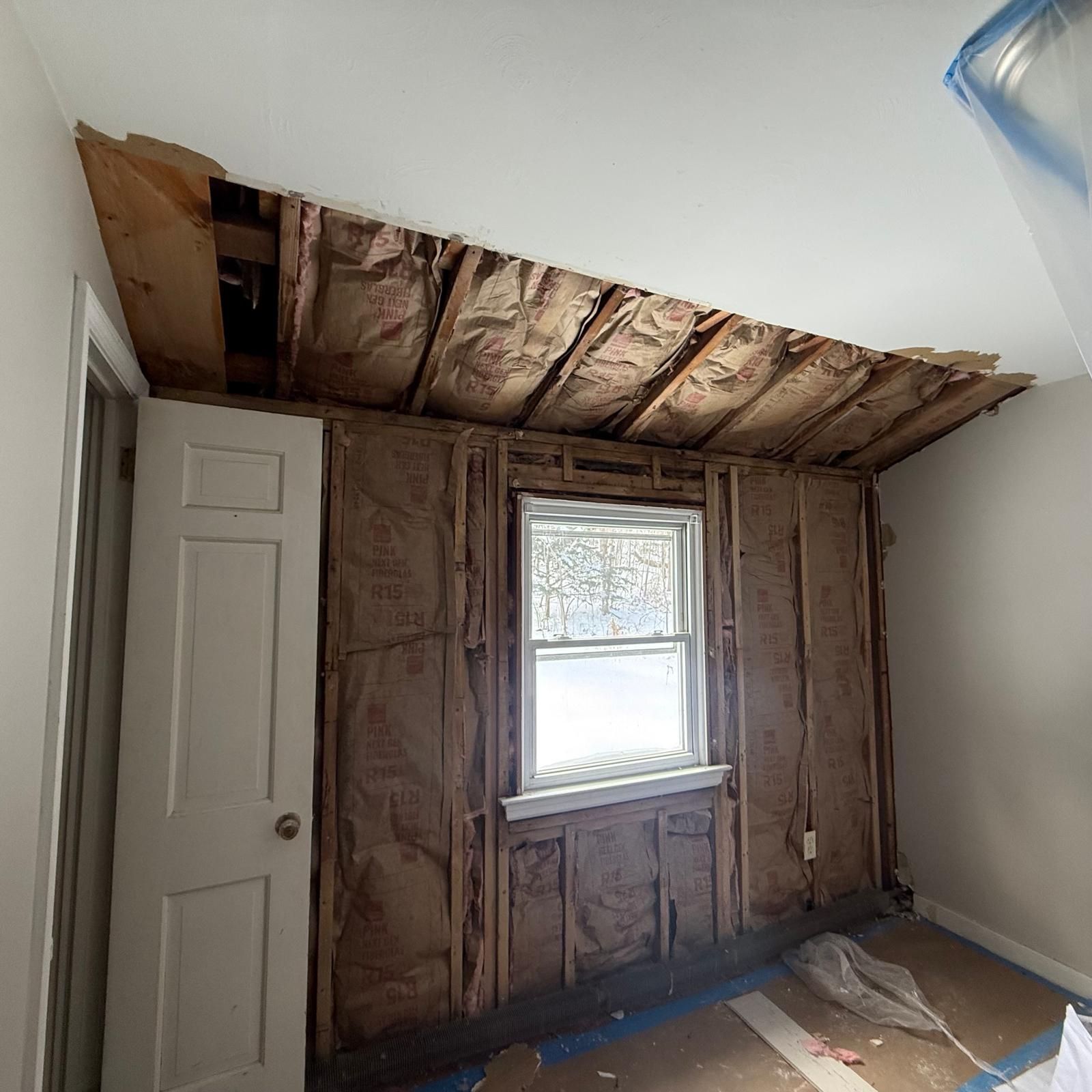 Partially demolished room with exposed insulation, damaged ceiling, and a small window wall section
