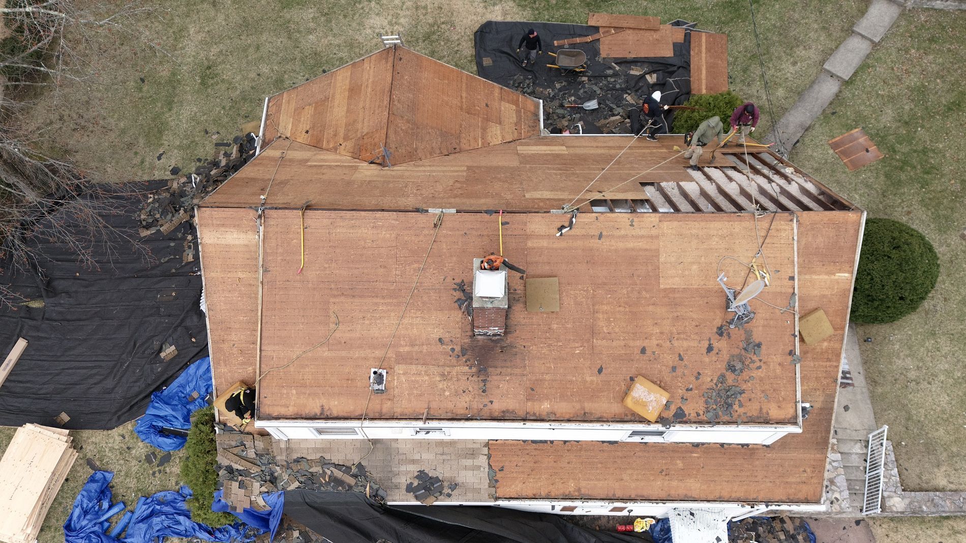 Aerial view of a roof under construction with exposed plywood, tools, and debris around the house.