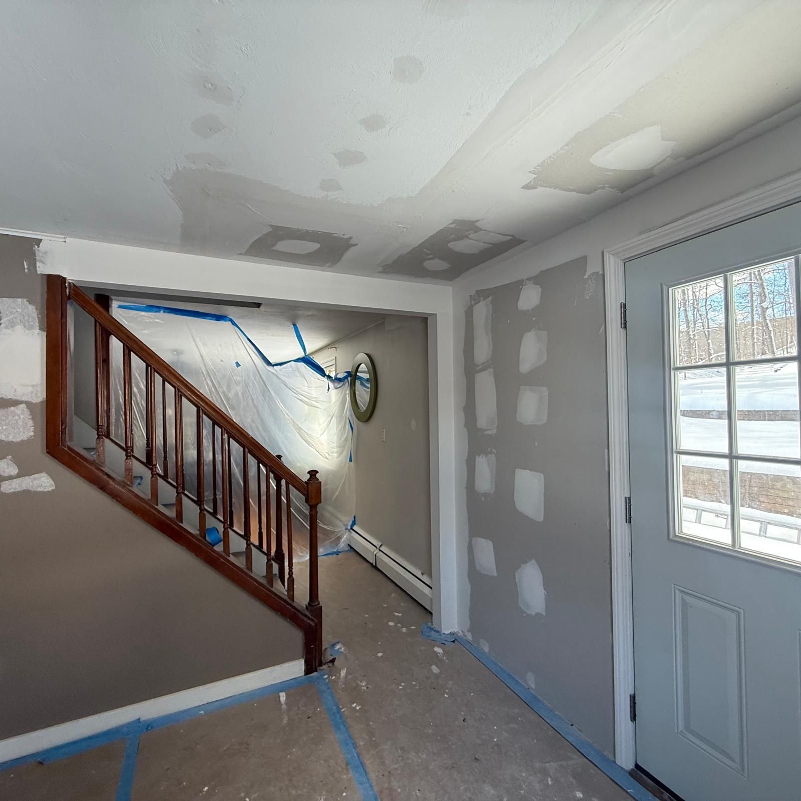 Partially renovated interior stairwell and entryway with drywall patches, taped floor, and a white door