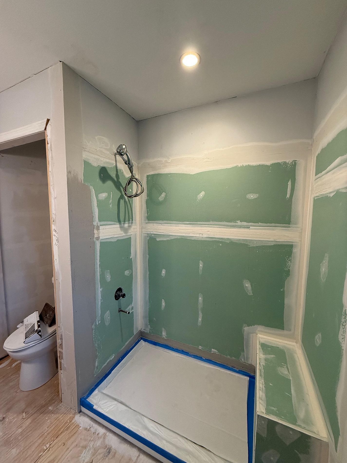 Bathroom under renovation with green drywall, shower pan, and toilet visible through doorway