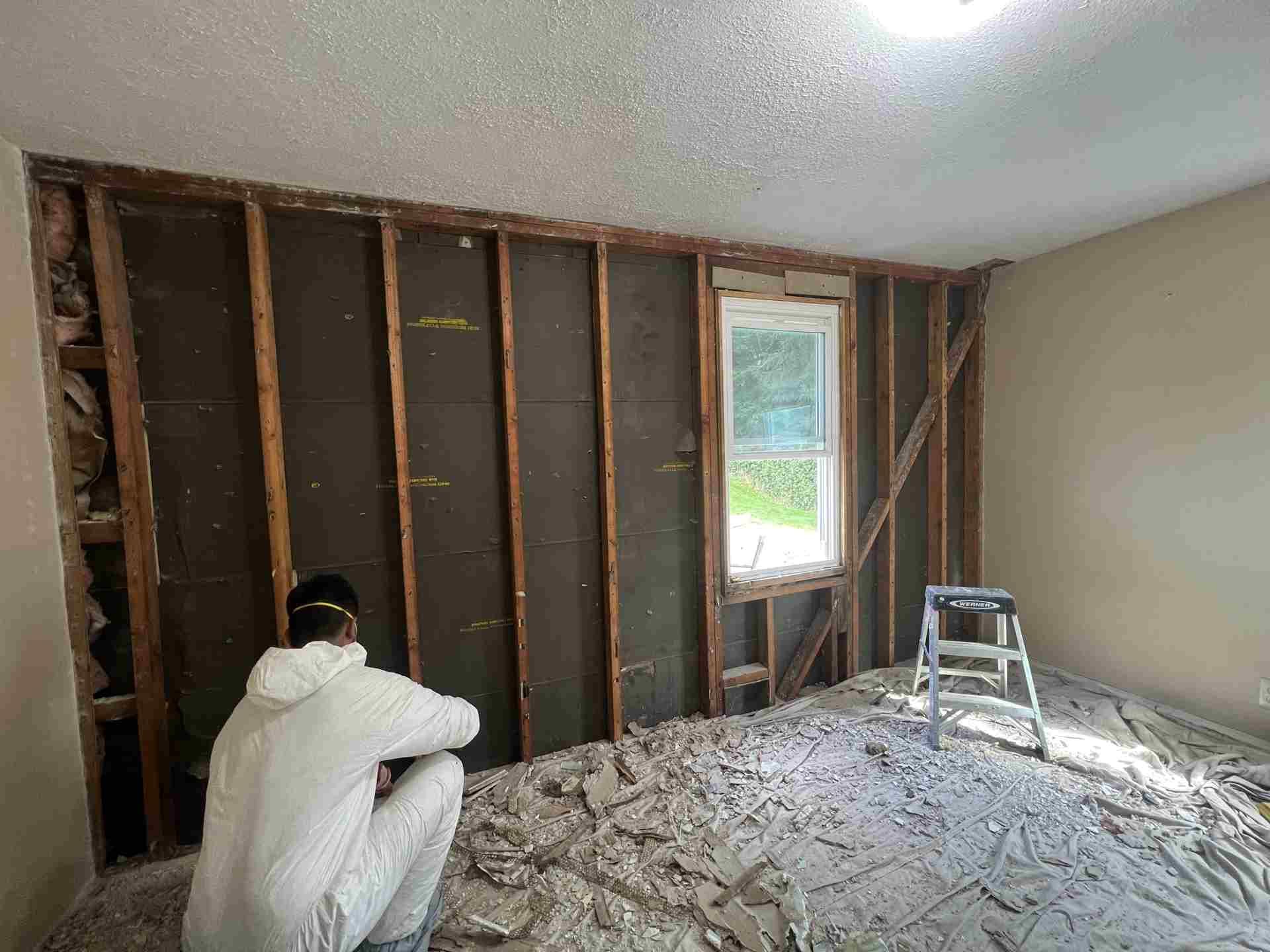 Person installing insulation in an unfinished room with exposed wall studs and a ladder.