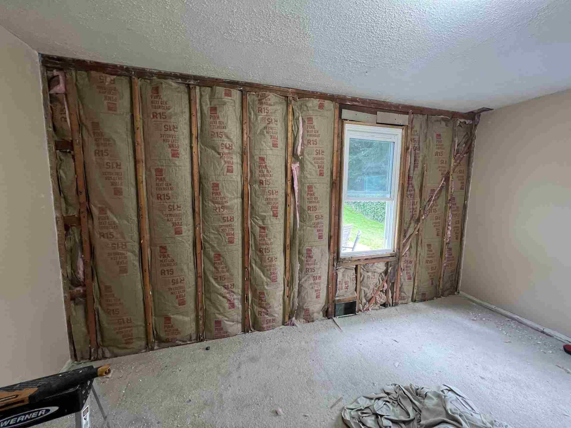 Partially renovated bedroom with exposed insulation, a window, and unfinished carpet removed from the floor