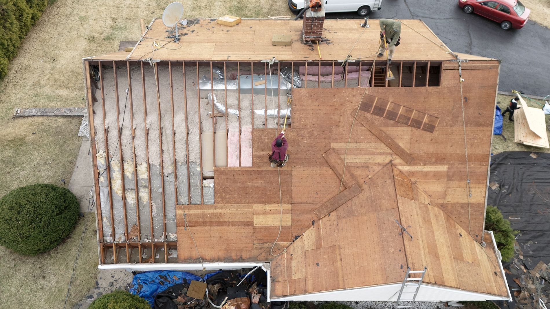 Aerial view of a house roof under construction with exposed wooden framing and brown shingles.