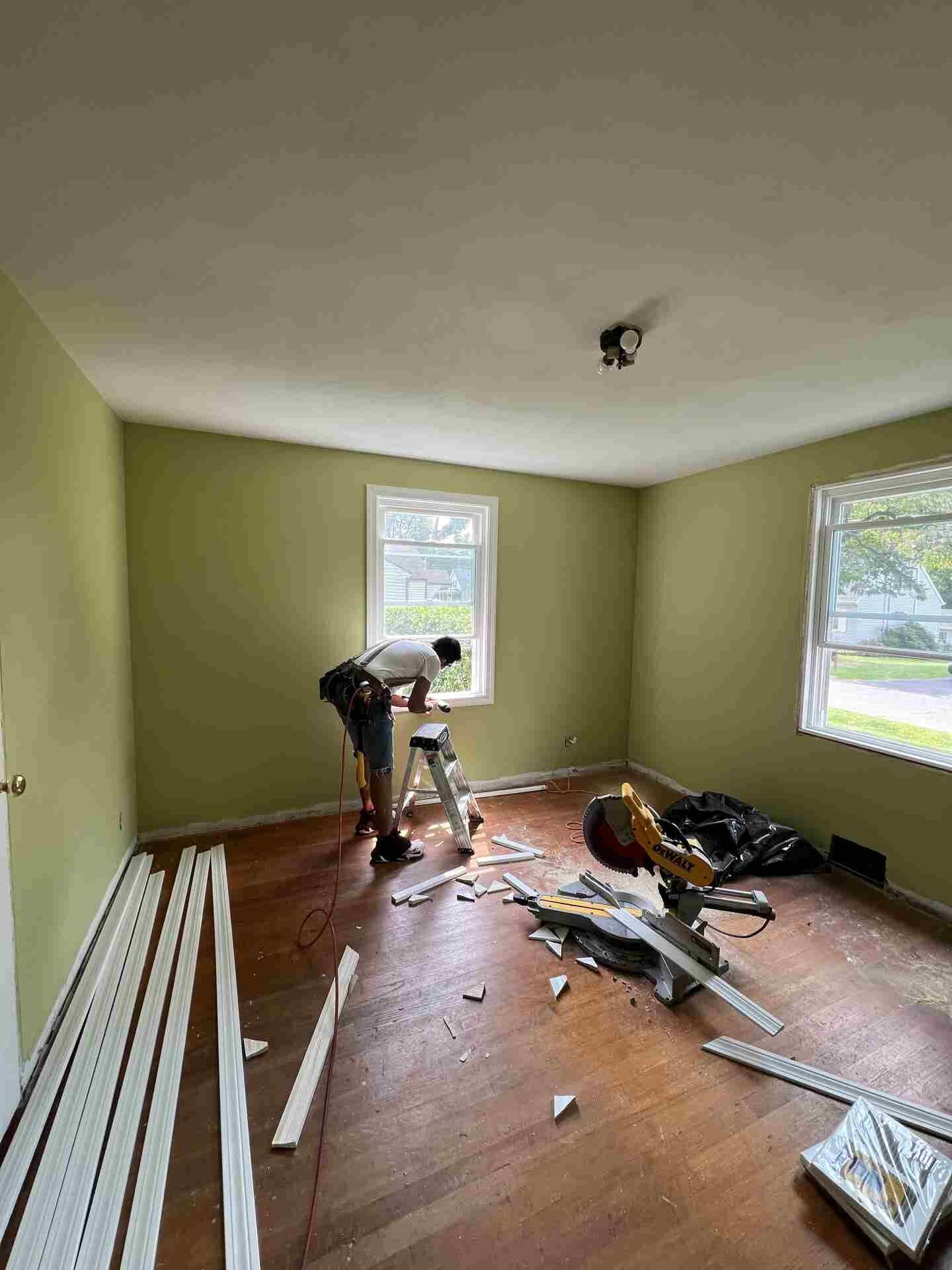 Worker installing flooring in an empty green room with tools and materials scattered on the floor.