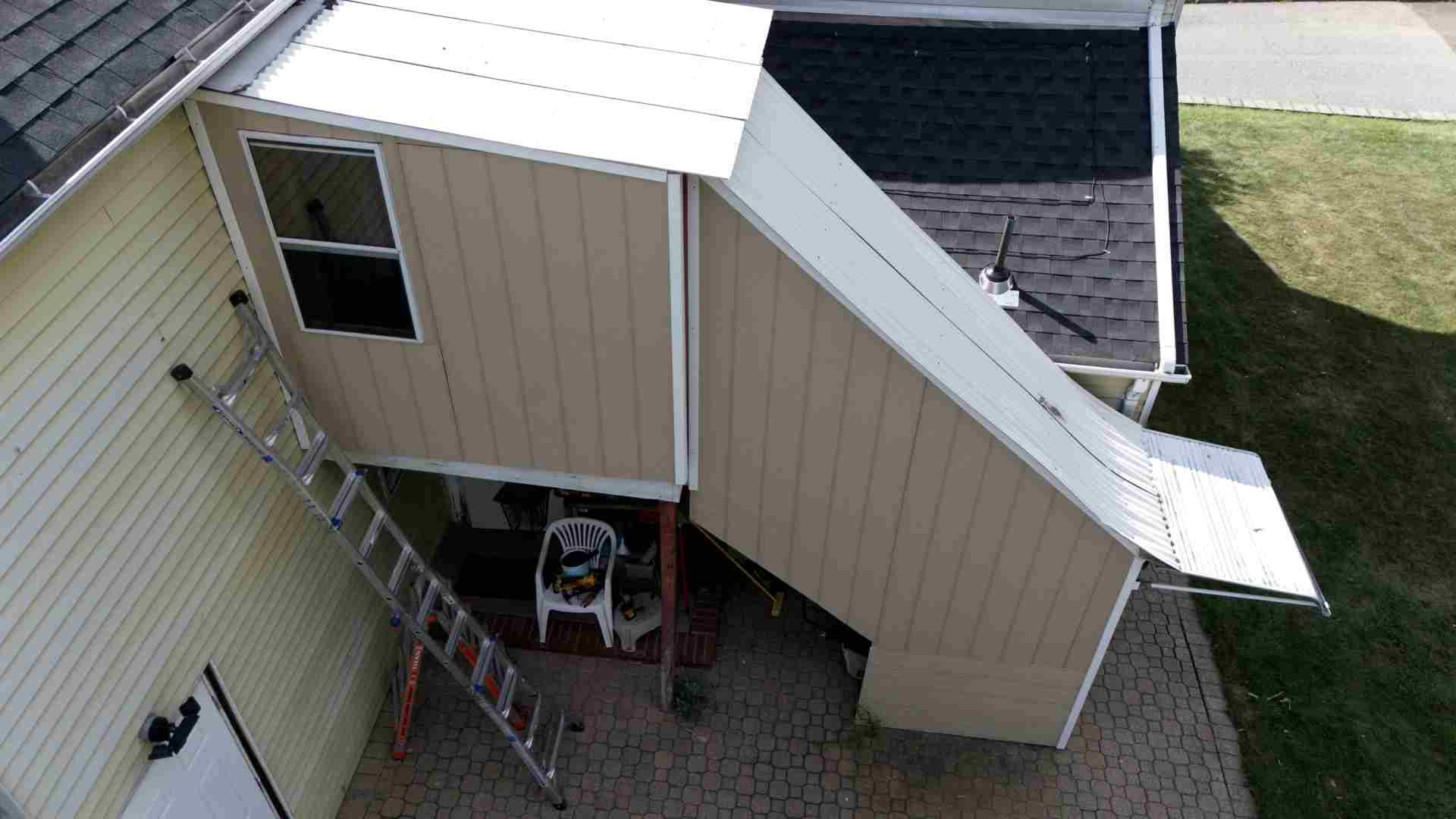House exterior with ladders leaning against beige siding and a covered roof section under repair