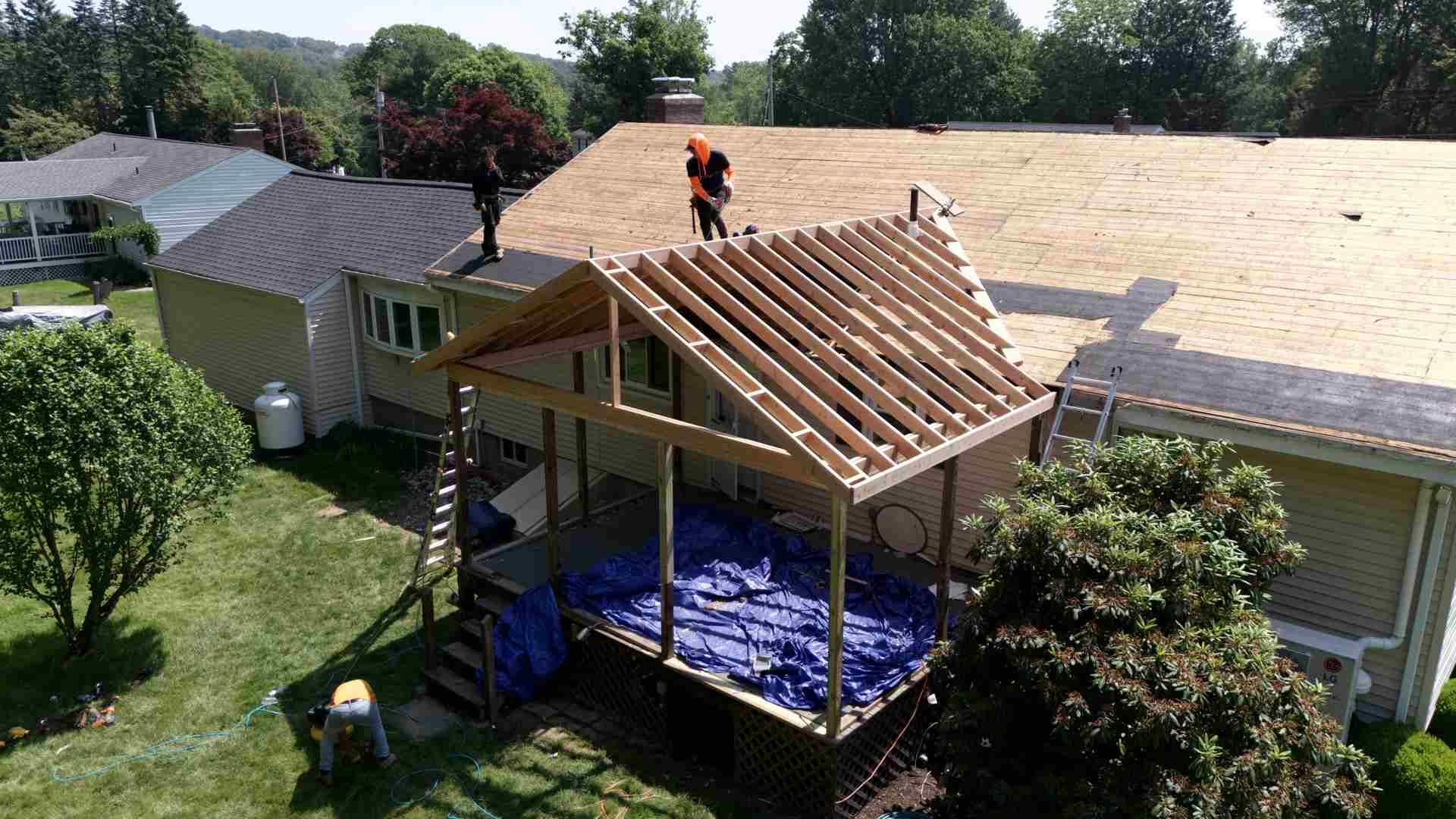 Person working on a new roof frame over a backyard deck beside a house