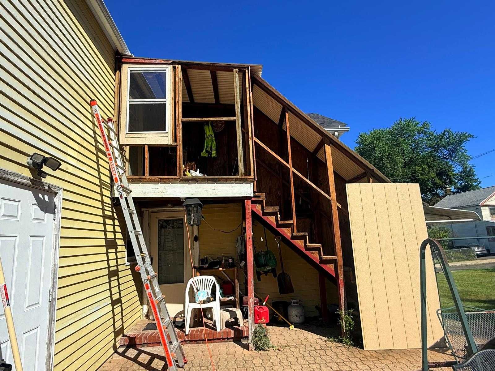 Outdoor staircase and enclosed landing attached to a house, with ladders and a chair below.