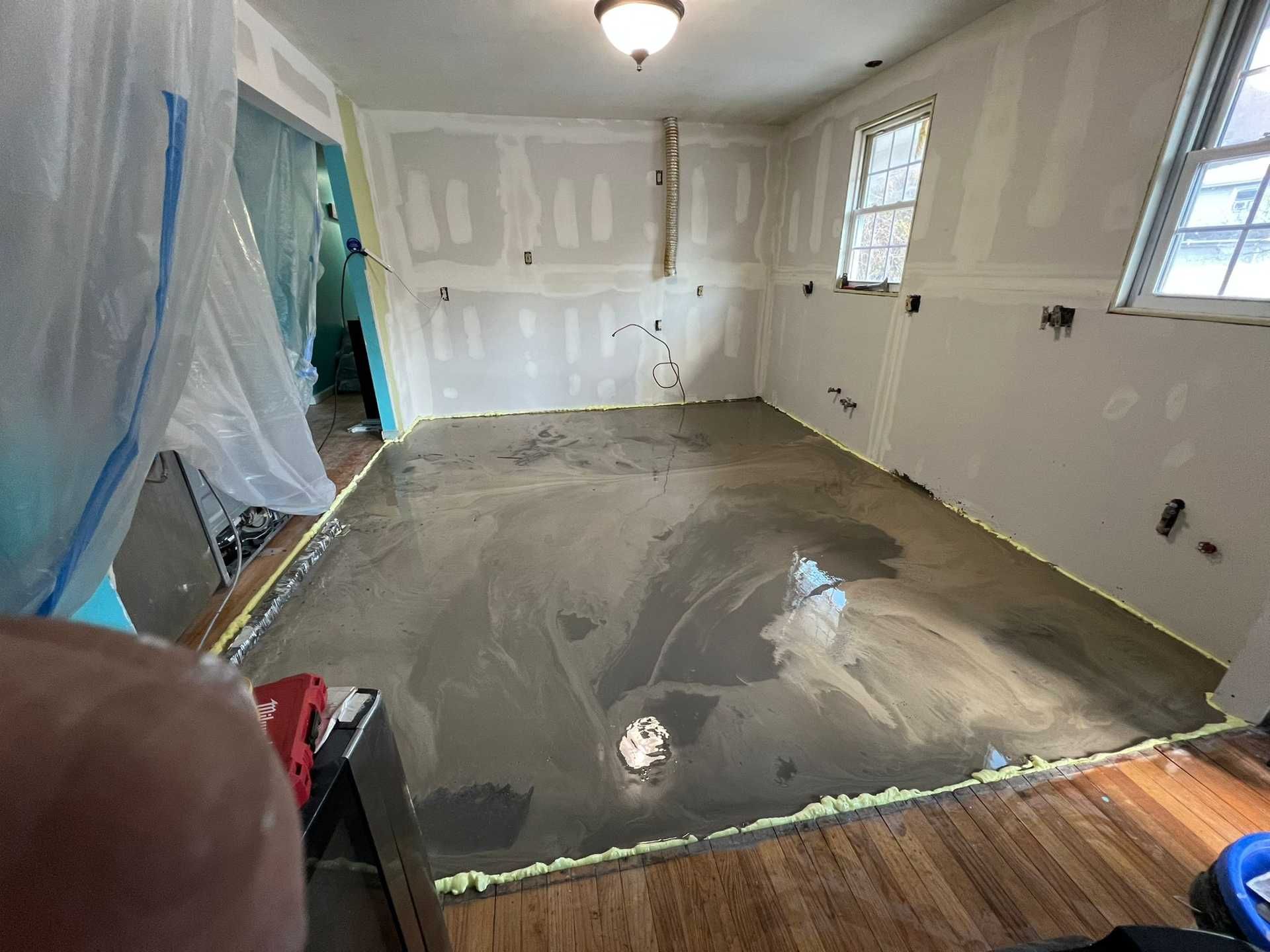 Partially finished room with wet concrete floor, white walls, and windows under renovation