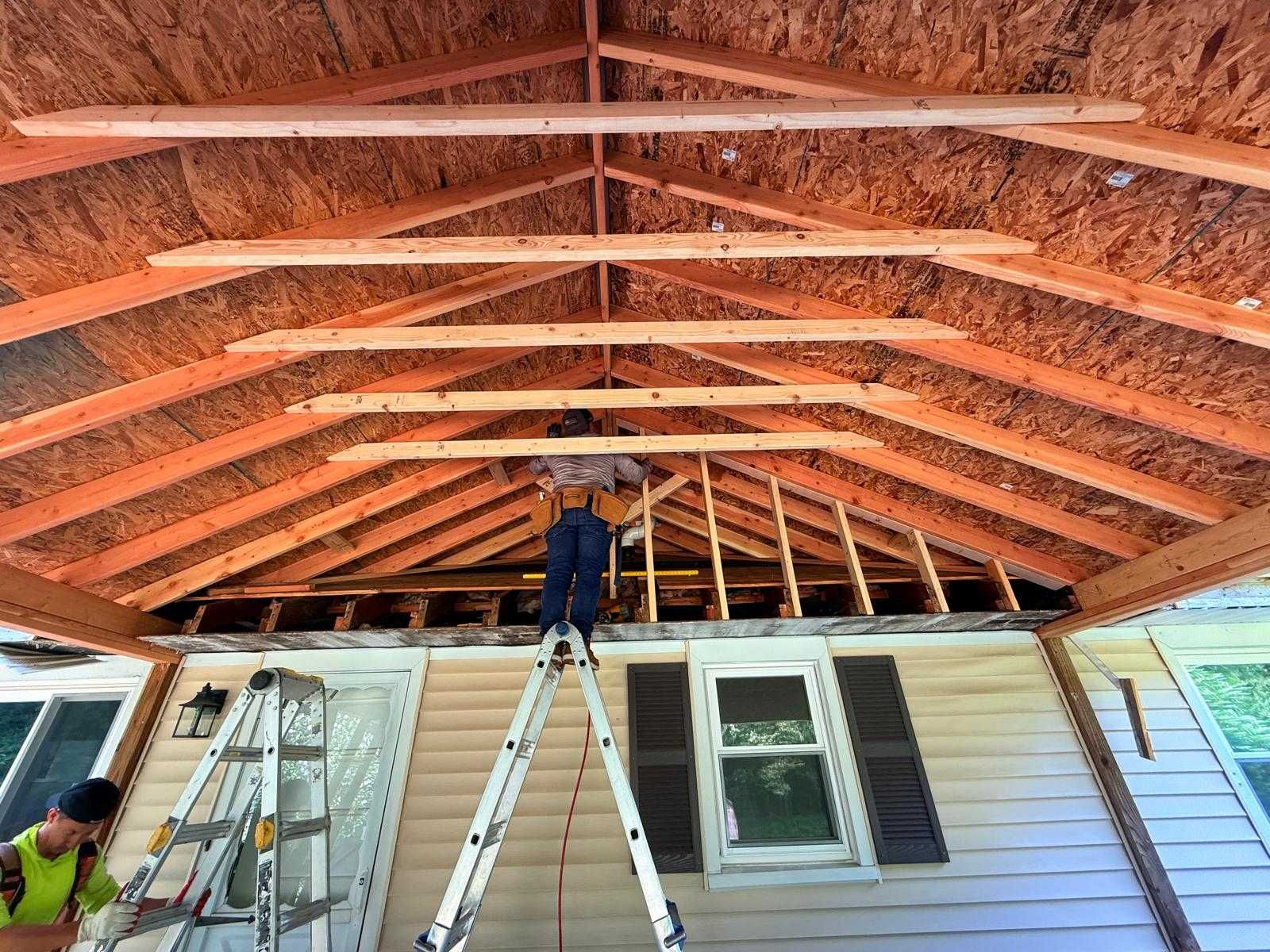 Workers building a roof frame over a house, with ladders and exposed rafters under construction