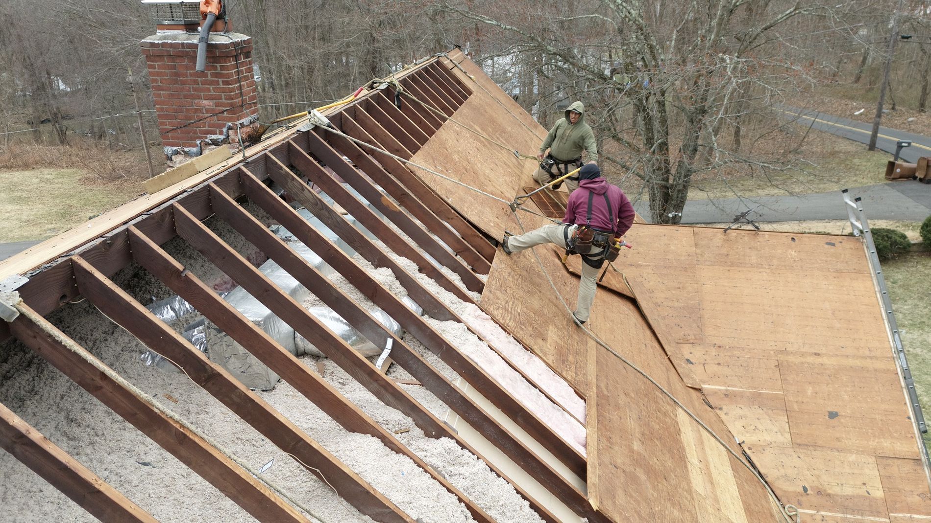 Worker repairing a steep roof with exposed rafters and plywood sheathing
