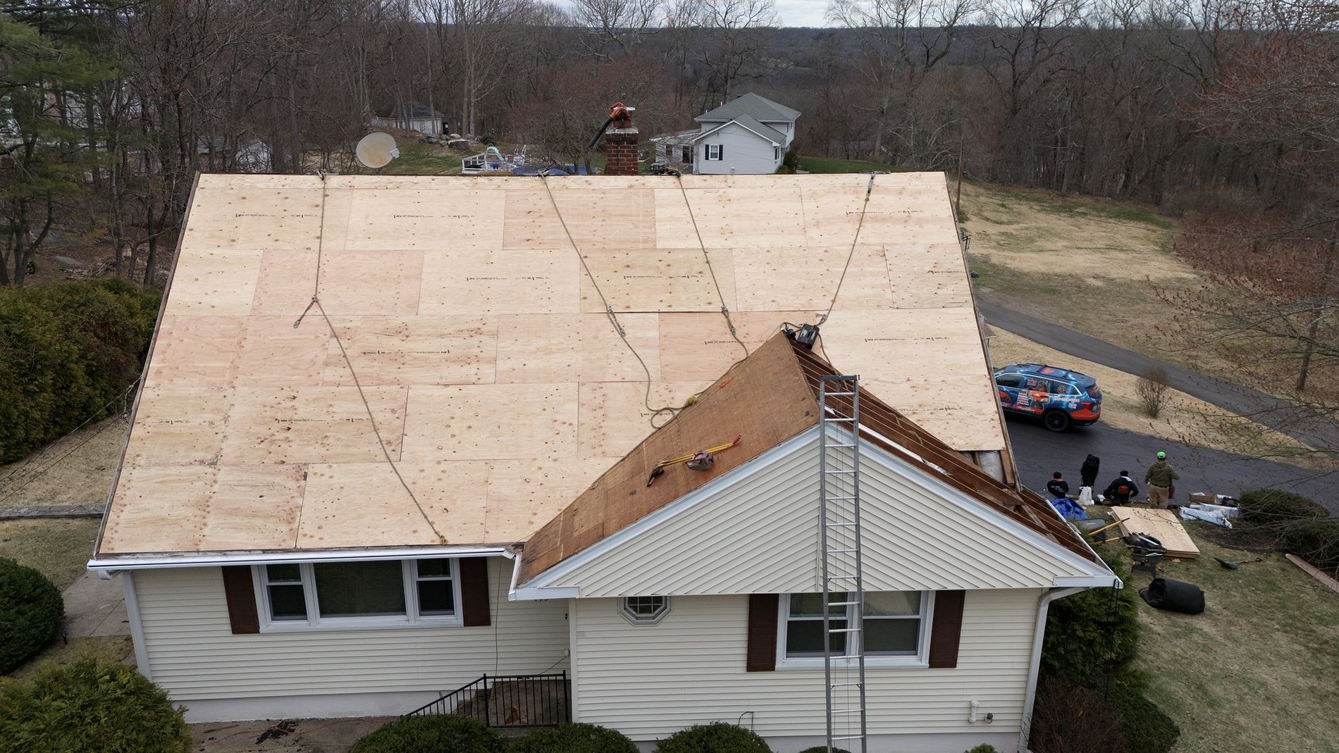 A house roof under construction with plywood sheathing and a smaller covered porch roof in front.