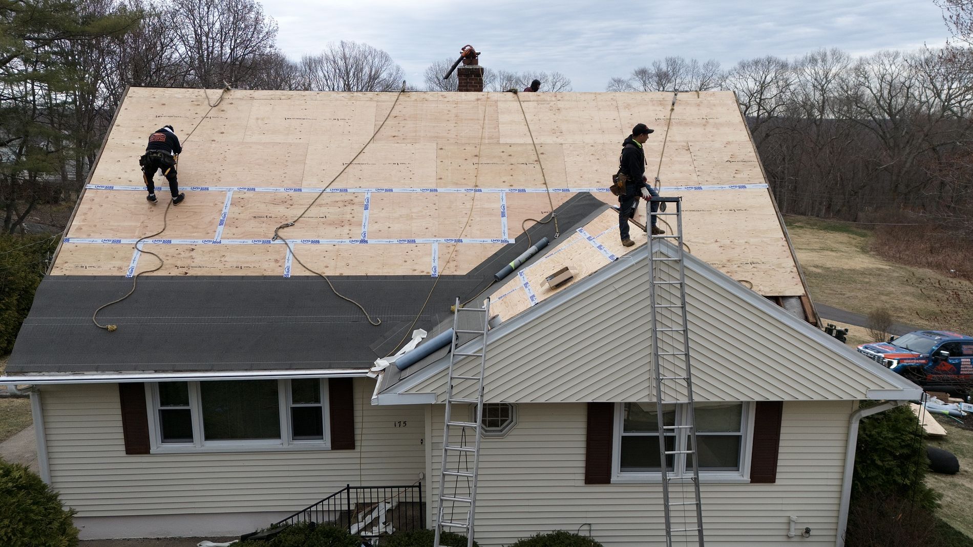 Workers installing plywood roofing on a house with a damaged front roof section