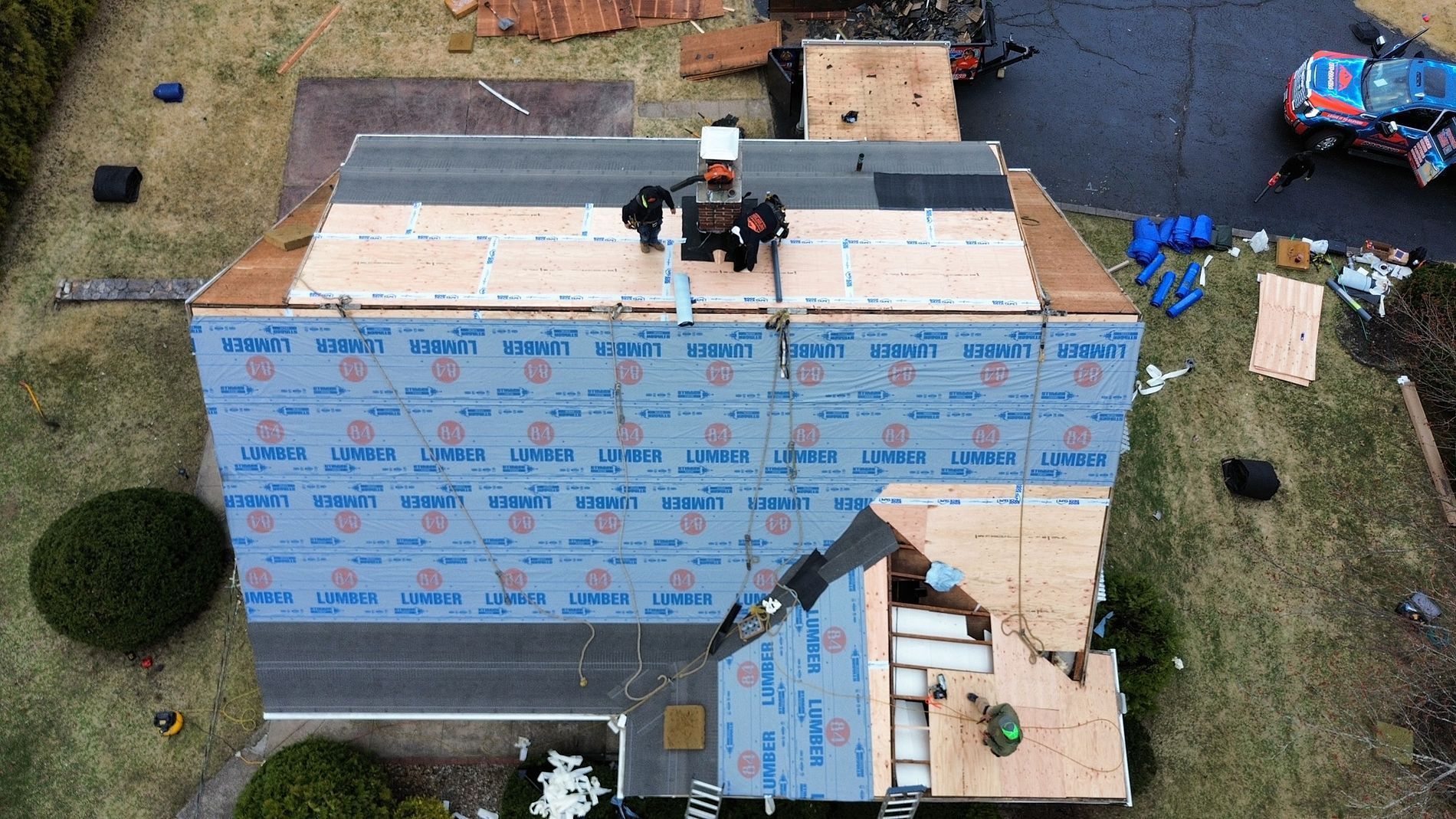 Aerial view of roofers installing blue roofing felt on a house under construction.