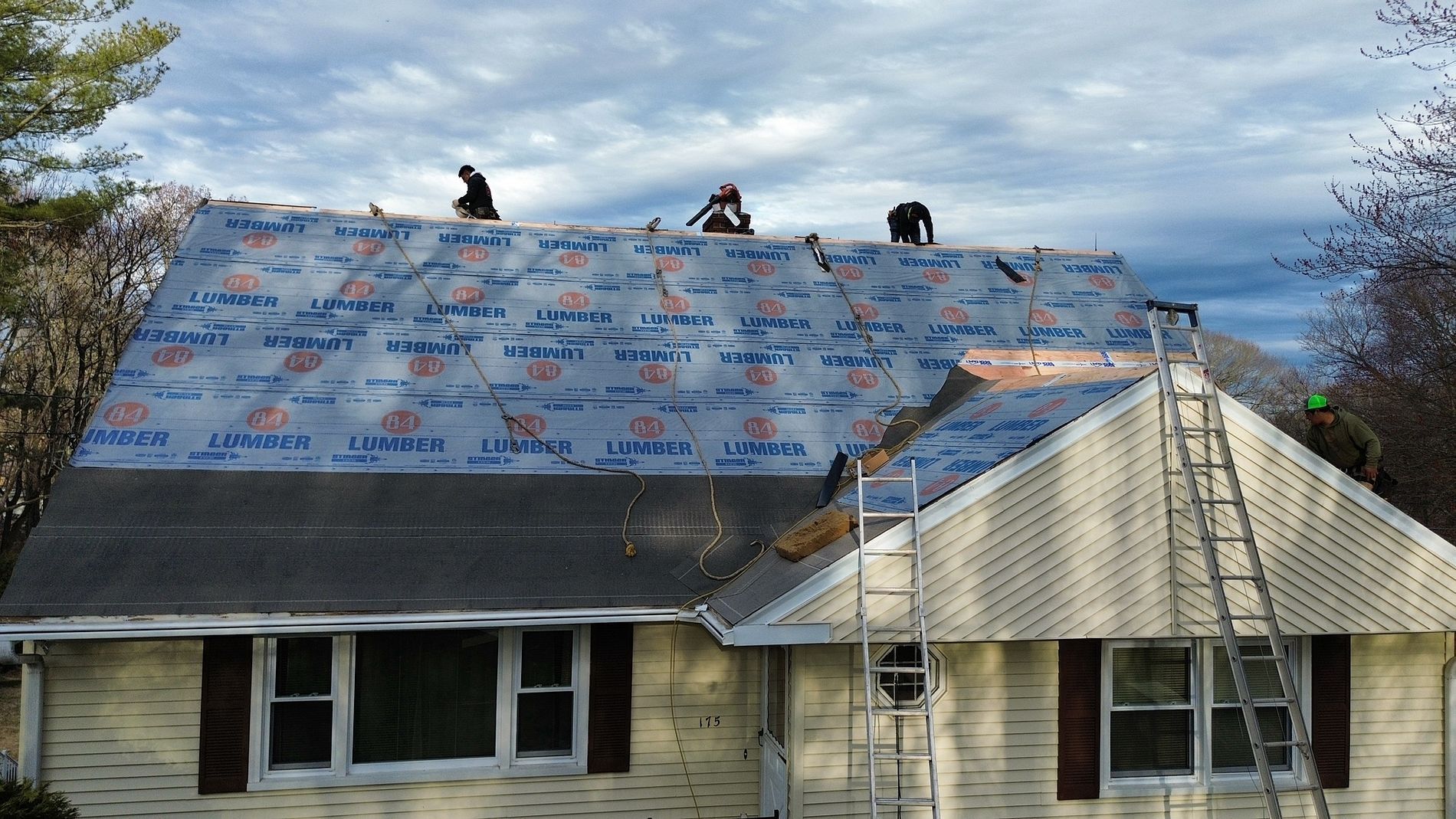 Workers reroofing a house with blue tarp under cloudy sky