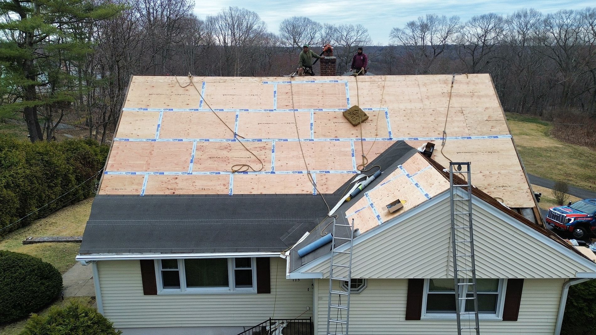 Roof under repair with exposed underlayment and two workers near the ridge on a suburban house