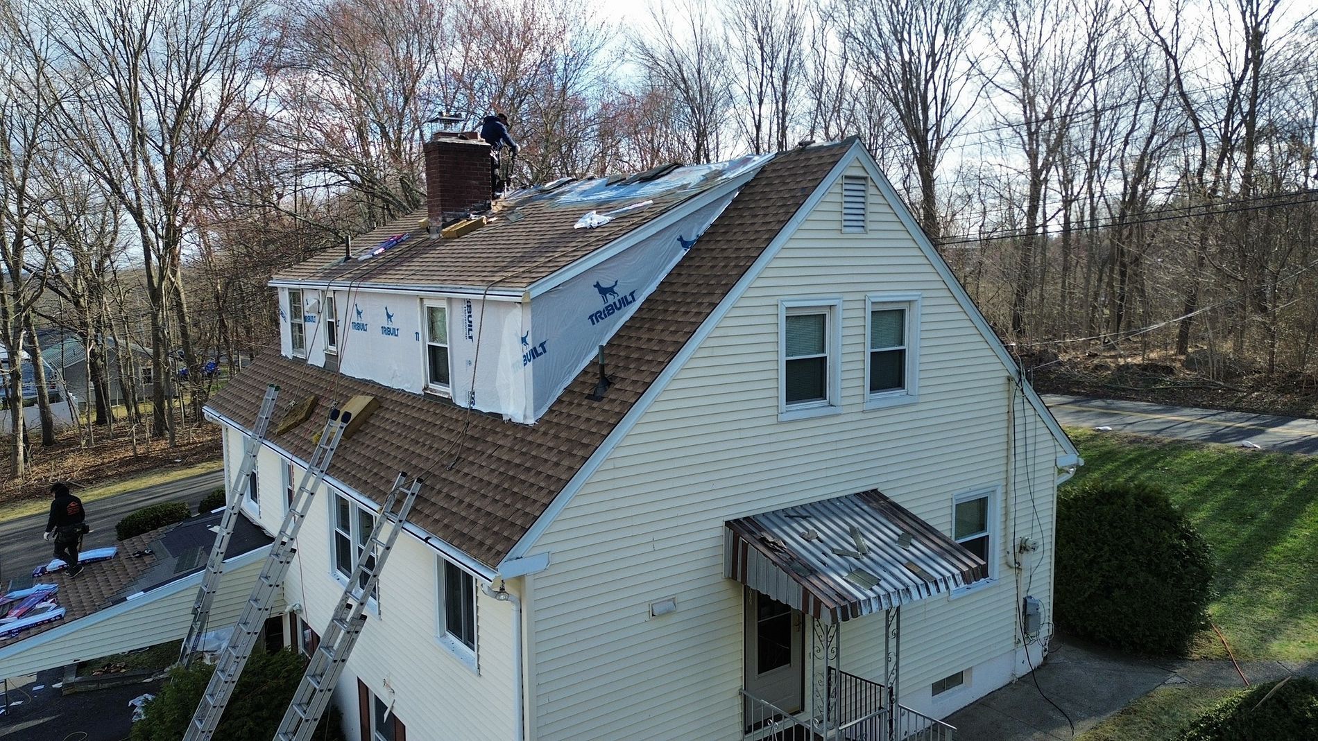 Aerial view of a white house with a brown roof and small porch, surrounded by leafless trees.