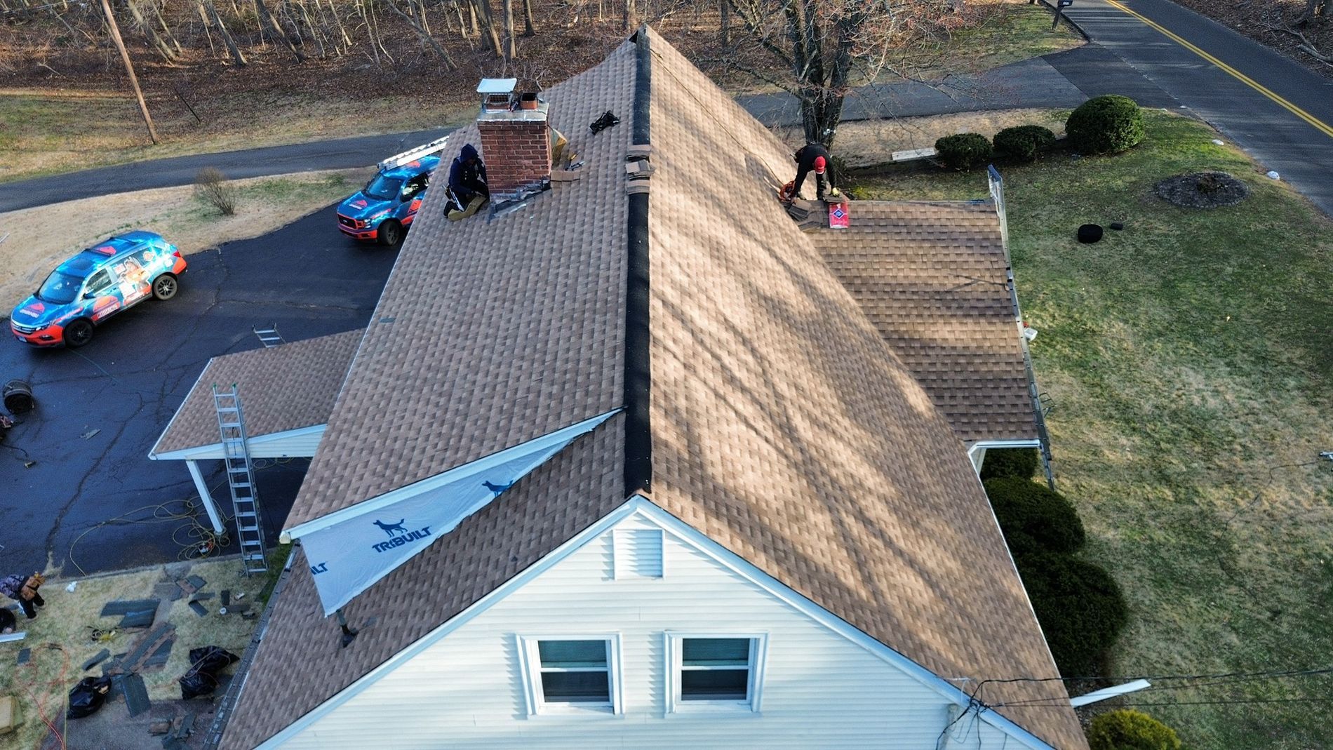 Aerial view of a house roof with a chimney, trampoline, and yard with a playset and parked items