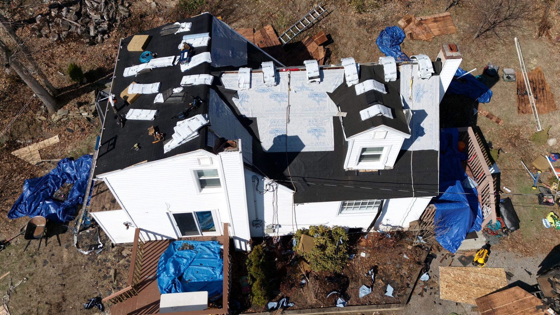 Aerial view of a house roof under repair, covered with black tarps and blue construction tarps.