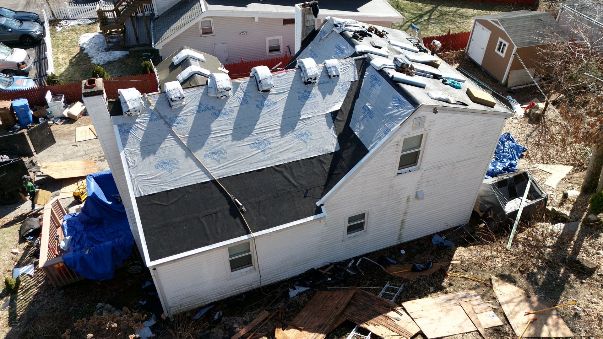 Damaged white house with missing roof shingles and debris around it after storm damage