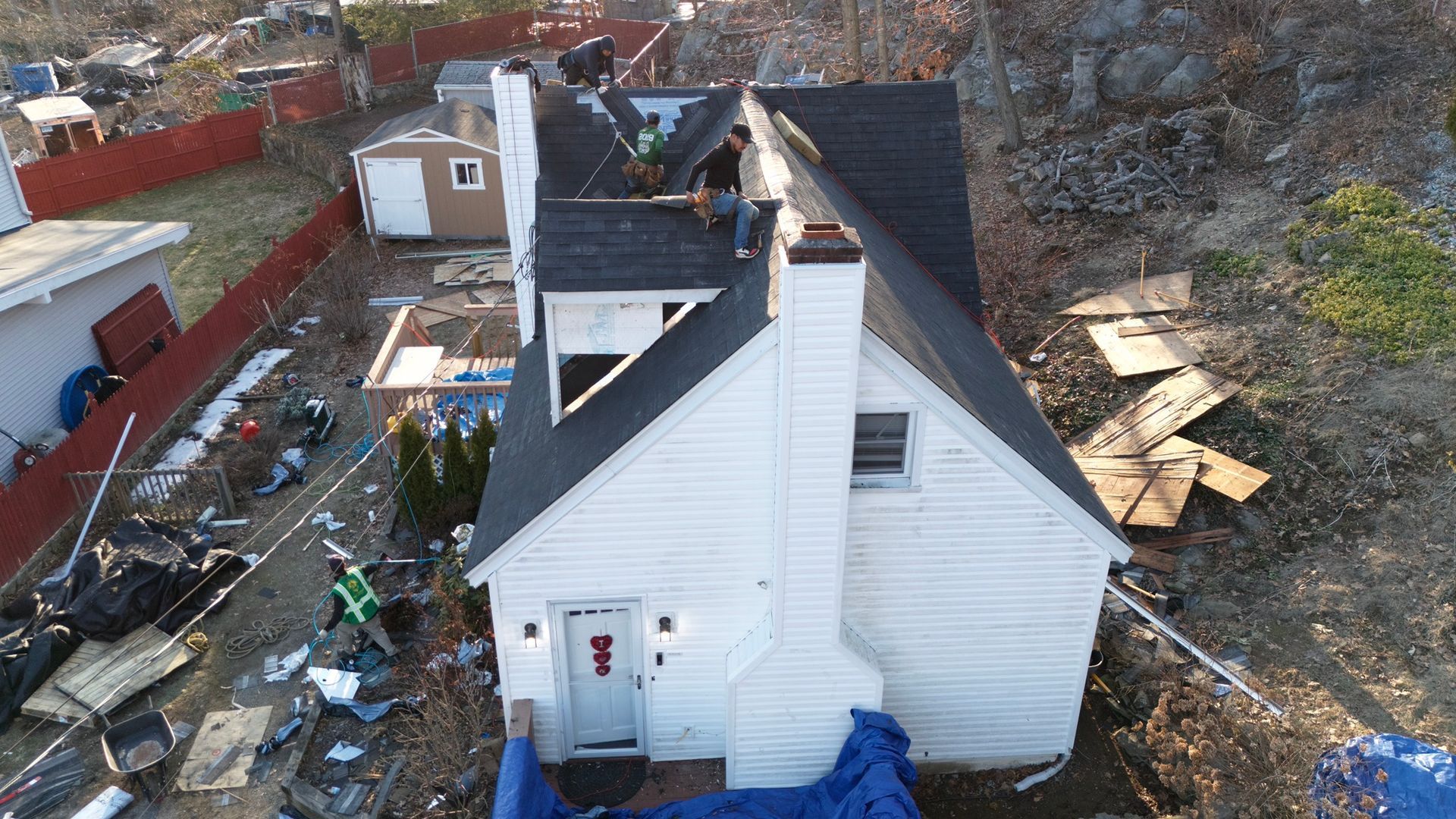 Aerial view of a white house with storm damage, debris scattered around and a damaged roof.
