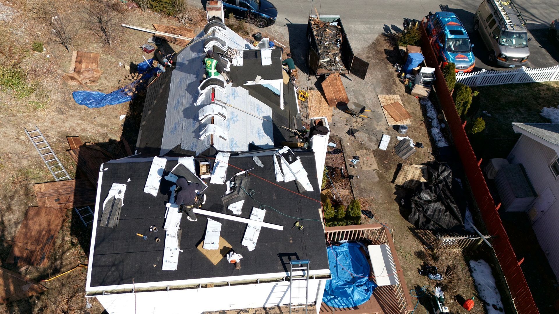 Aerial view of a damaged house roof with debris and workers beside parked vehicles and trucks