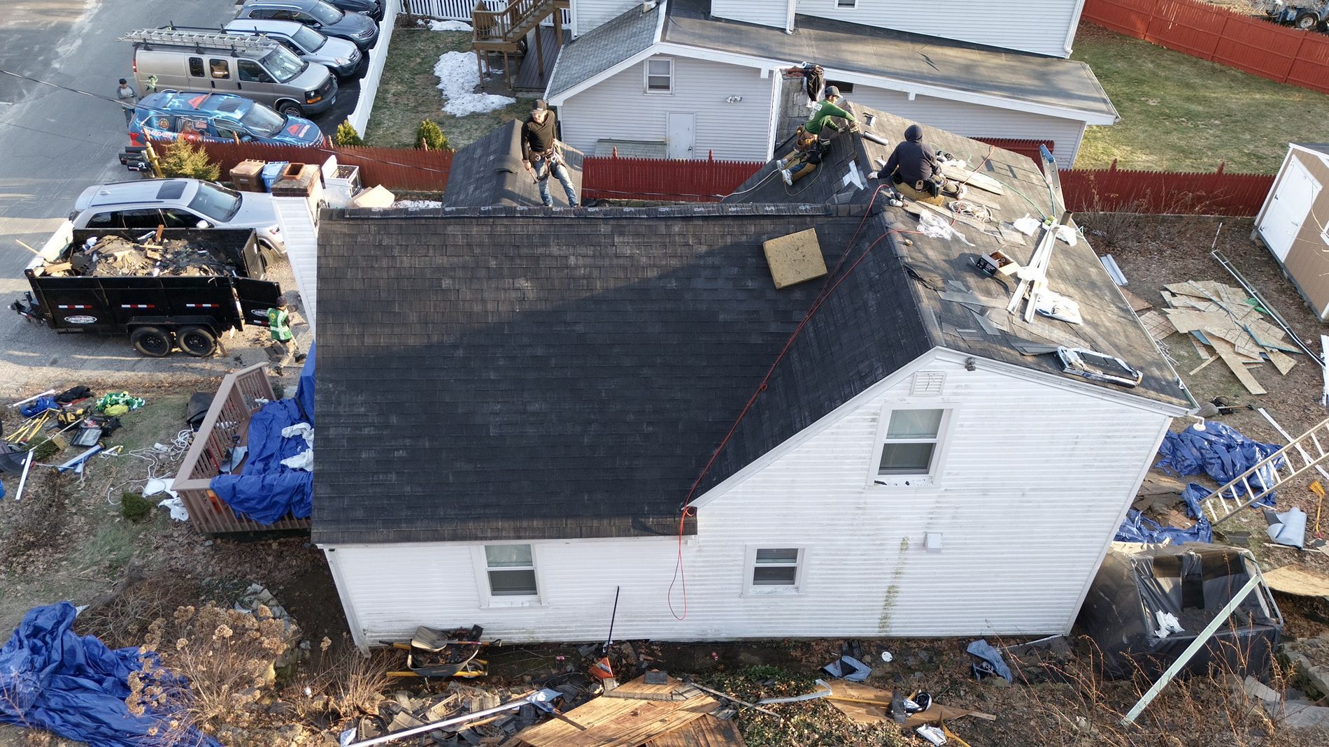 Aerial view of a house with roof damage and debris scattered around the yard and nearby structures