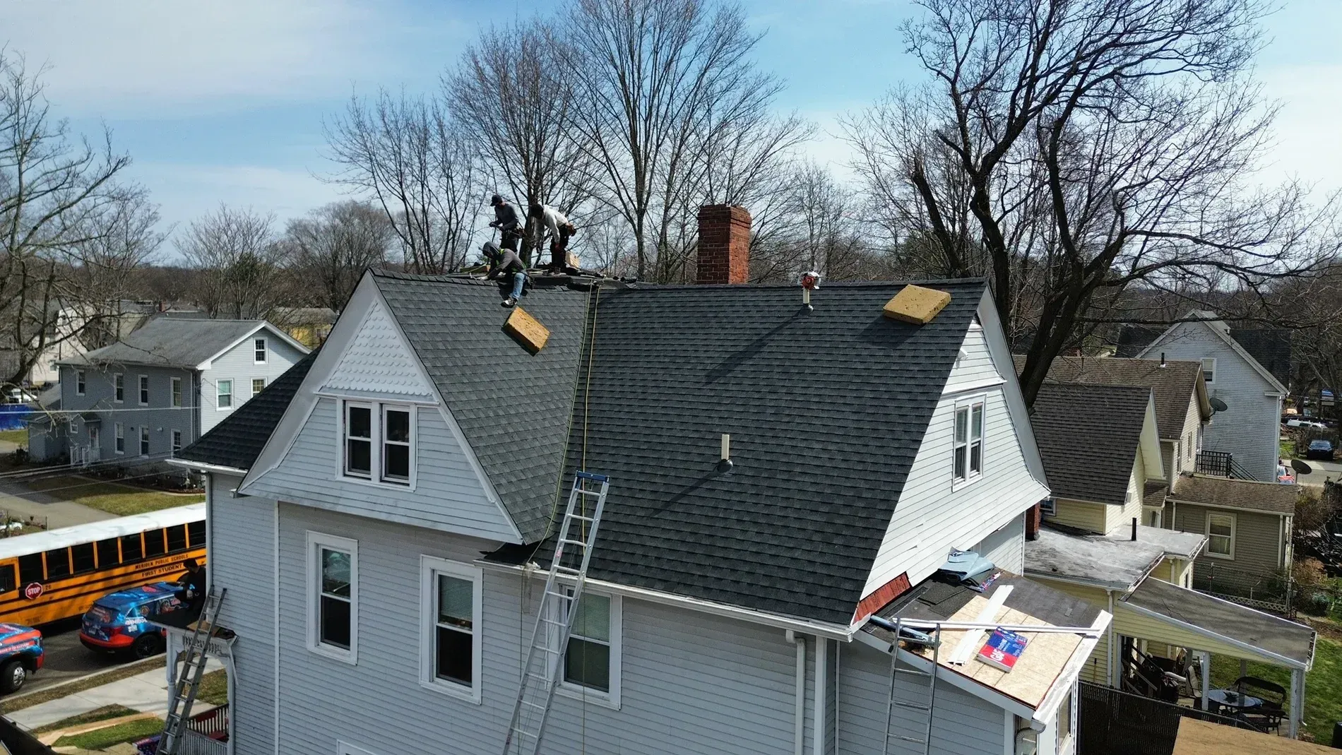 Workers repairing a gray house roof with a cherry picker in a suburban neighborhood