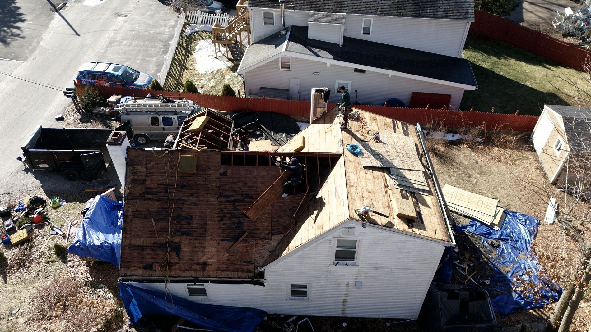Aerial view of a house with severe roof damage and blue tarps after storm repairs