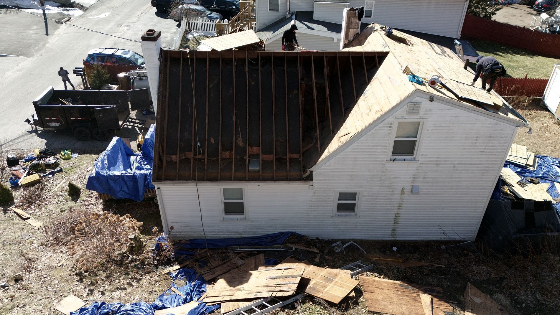 Damaged white house with a torn-off roof, exposed framing, and debris scattered around the yard