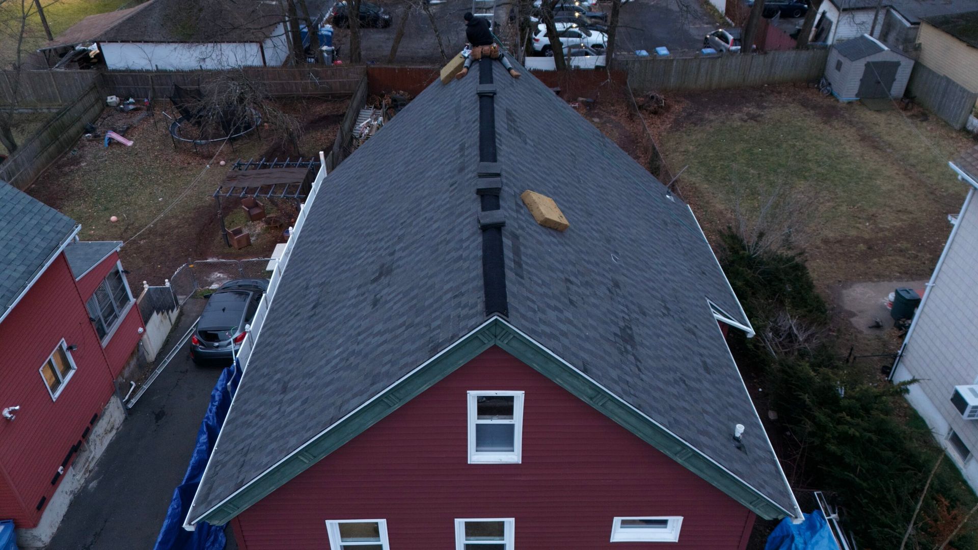 Aerial view of a red house with a dark roof and a chimney in a residential neighborhood