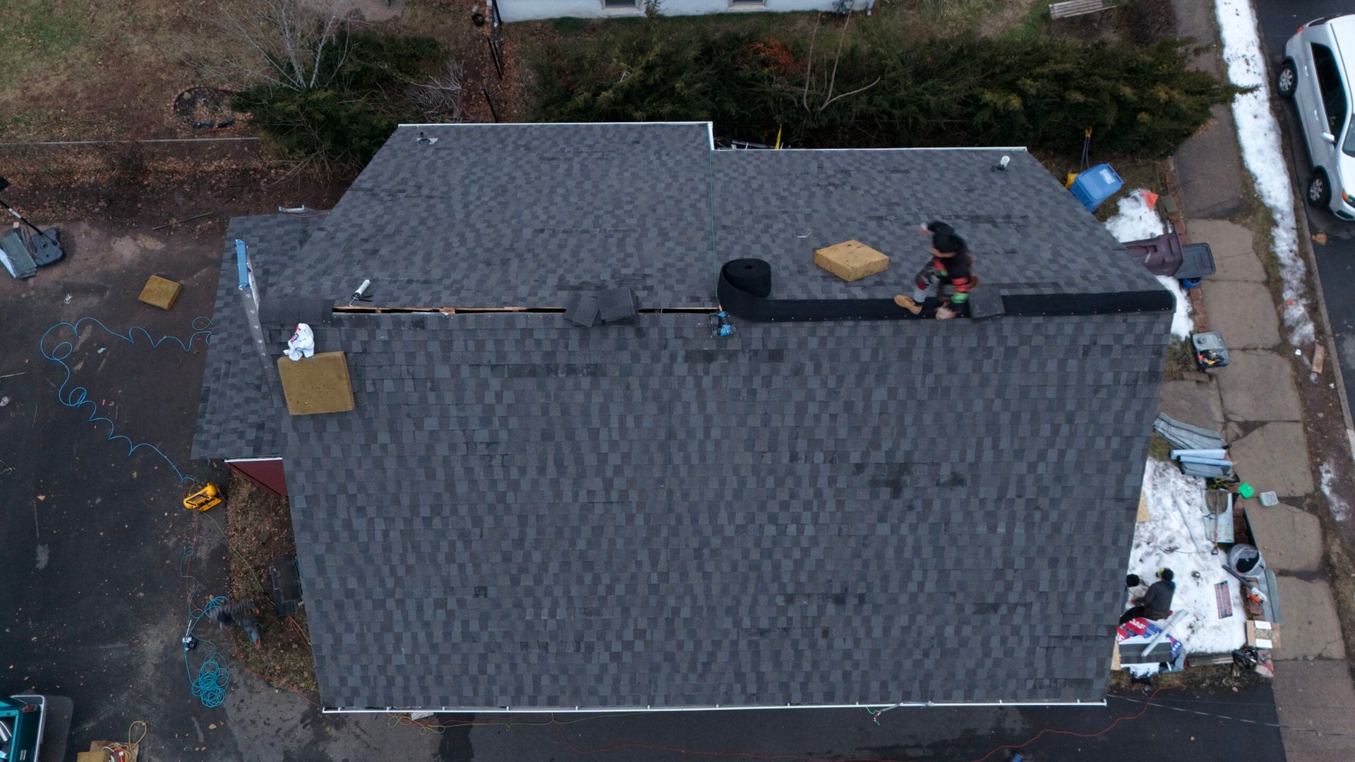Aerial view of a gray roof with two workers and roofing materials in a residential yard