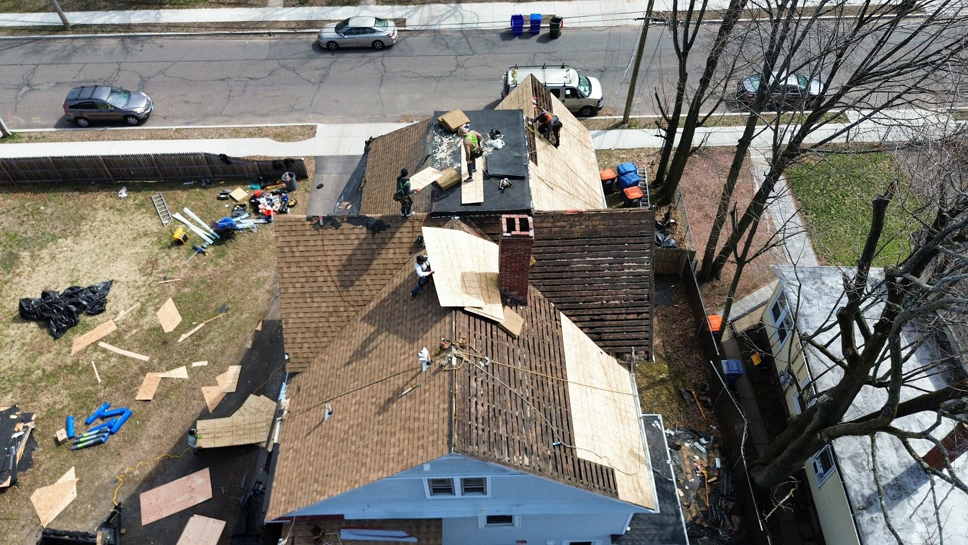 Aerial view of a roof under repair with missing shingles and construction materials beside a road