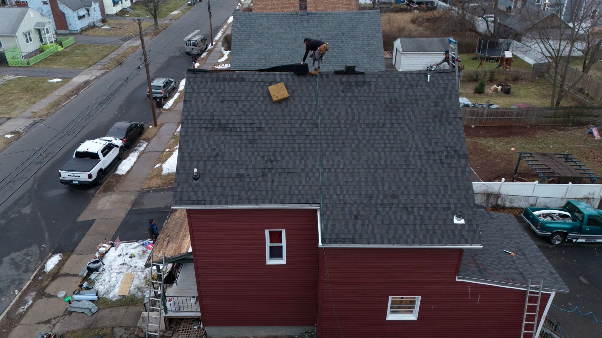 Aerial view of a red house with a damaged roof, with people working on repairs.