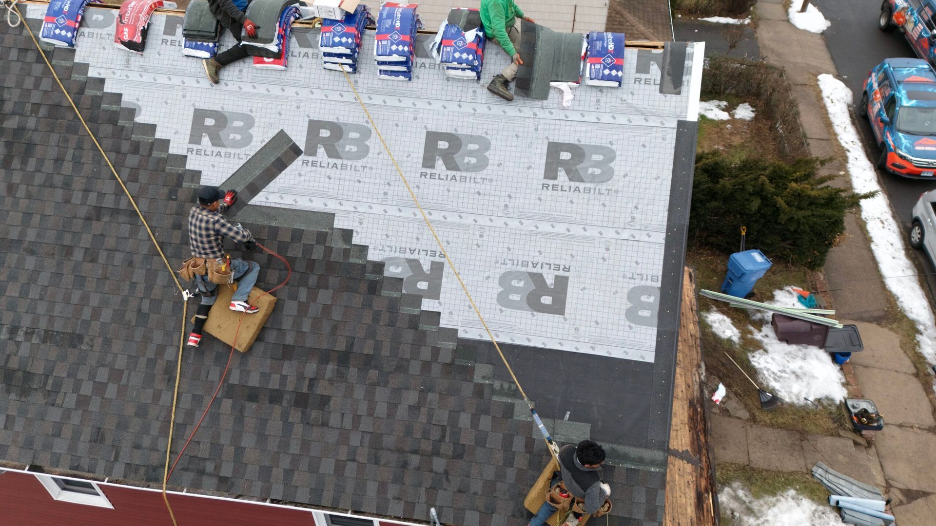 Roofers installing gray shingles on a steep residential roof next to a section of black shingles