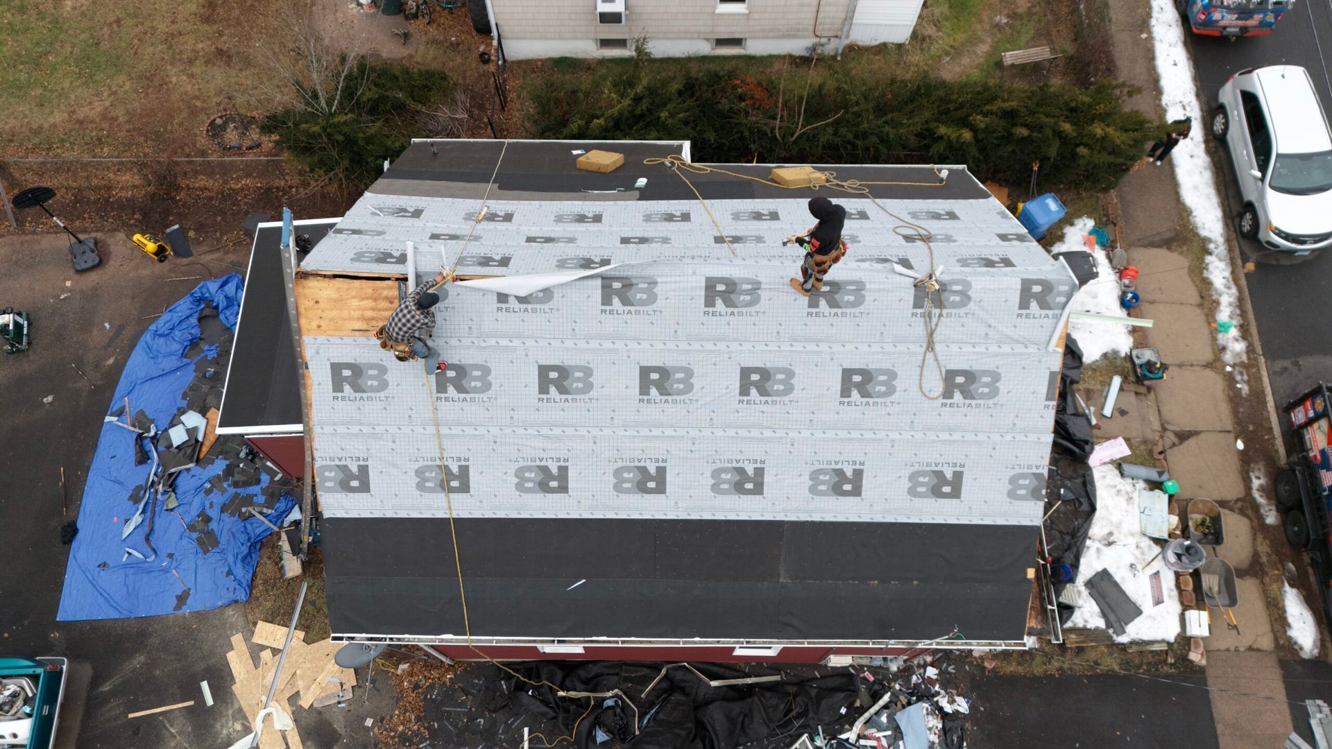 Aerial view of workers installing a new roof on a house, with roofing materials and debris around it.