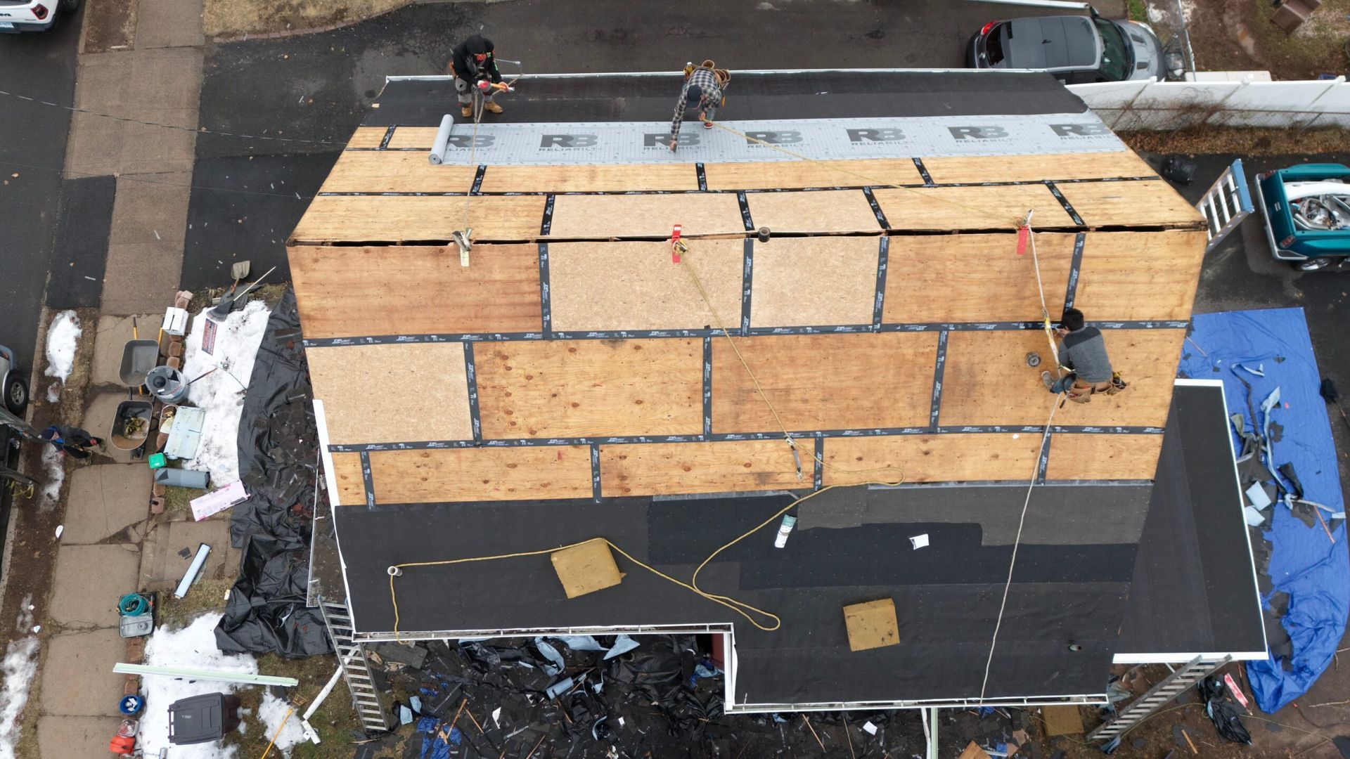 Workers on a rooftop secure large wooden crates or panels amid construction debris.