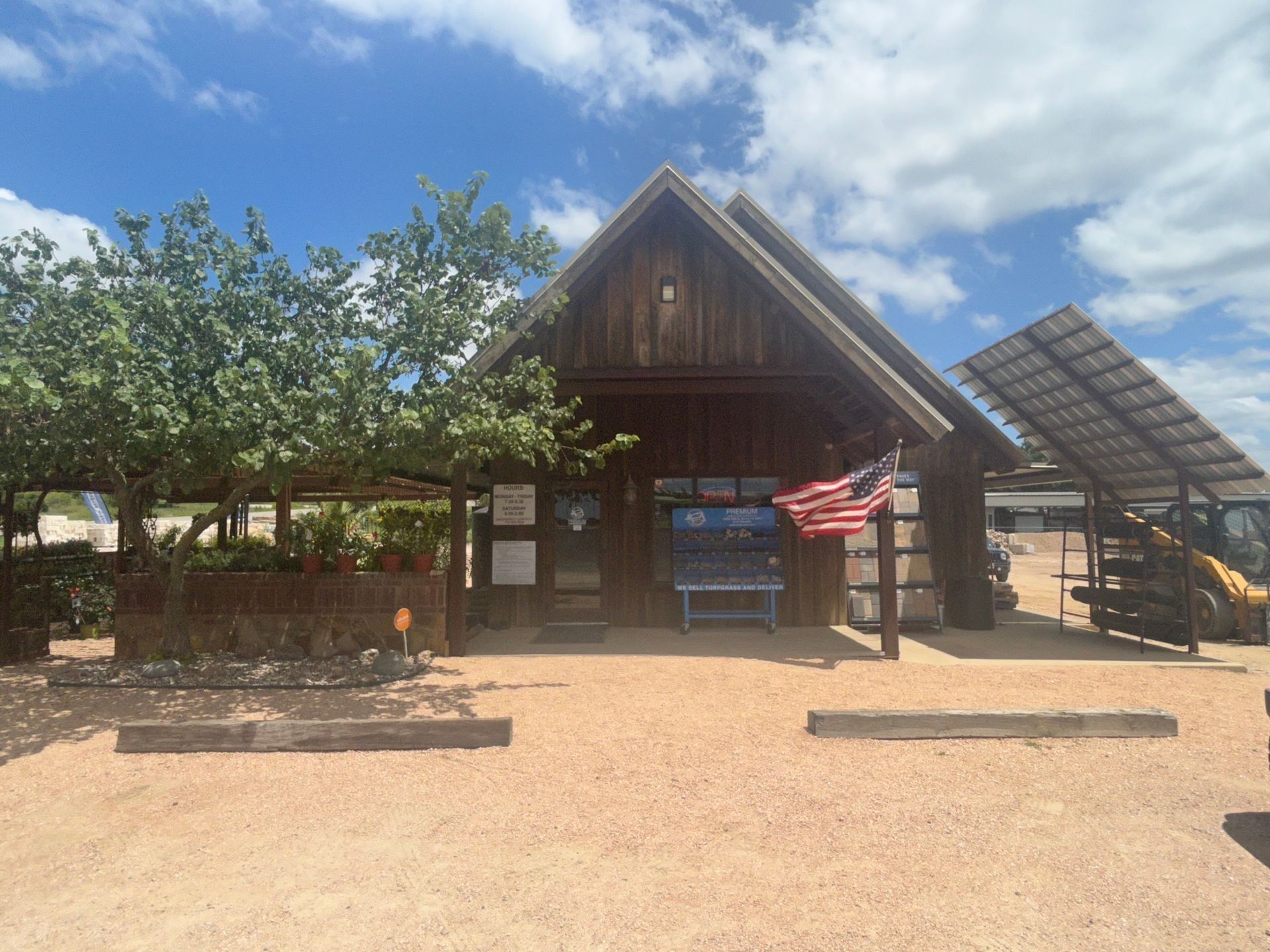 Wooden building with solar panels, American flag, and gravel parking area under a blue sky.