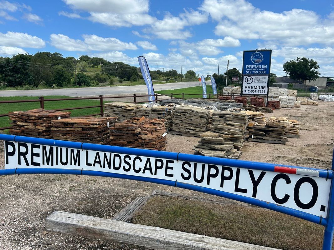 Premium Landscape Supply Co. sign with displays of stone and bricks under a blue sky.