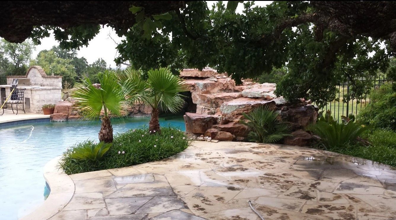 Swimming pool with rock waterfall feature, palm trees, and stone patio.