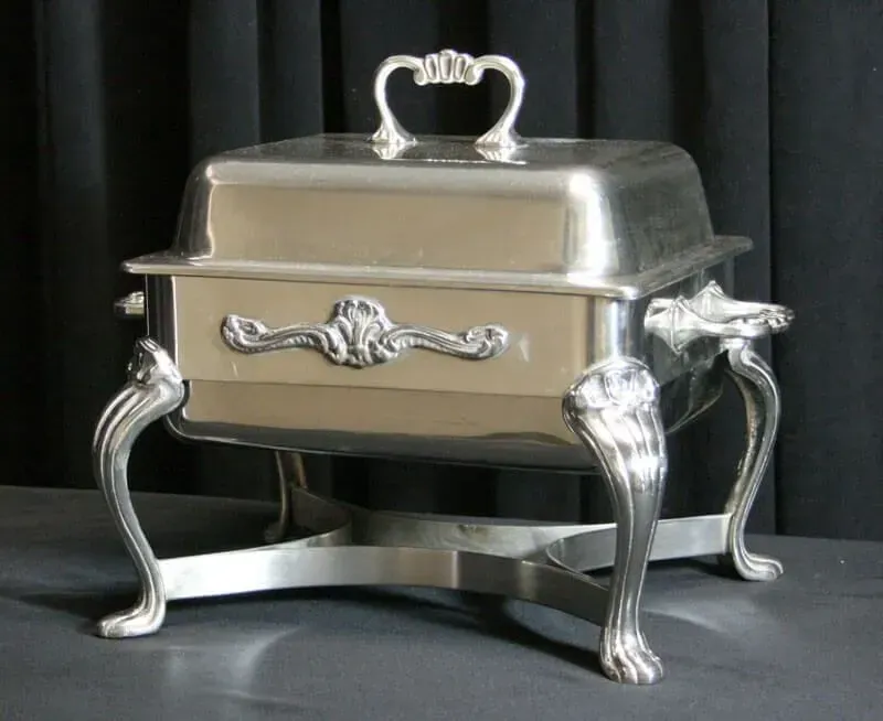Ornate silver serving dish with curved legs and lid on a dark background