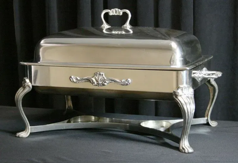 Silver chafing dish with ornate legs and lid on a black background